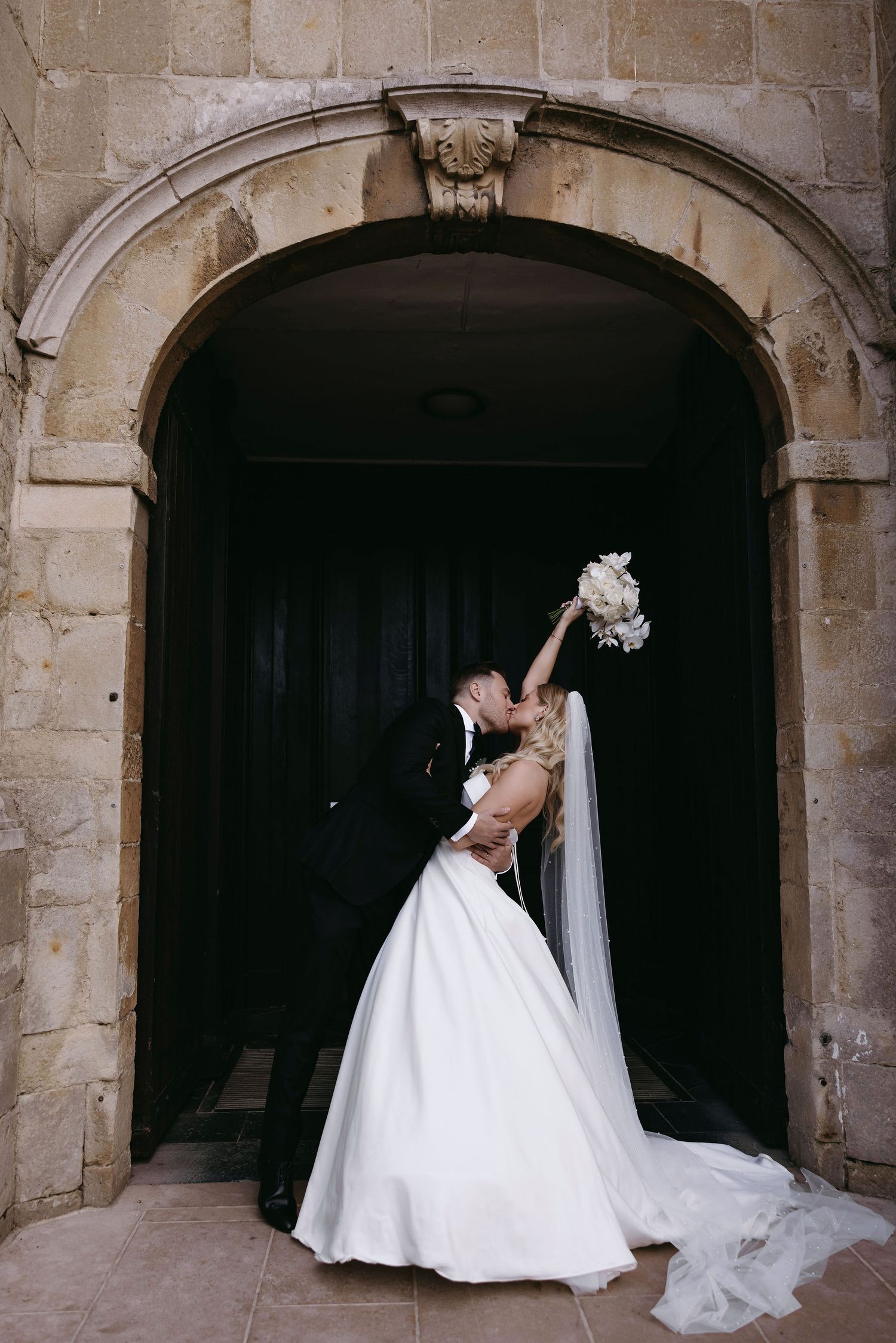 Romantic wedding portraits under stone archways showcasing a flowing white wedding dress.