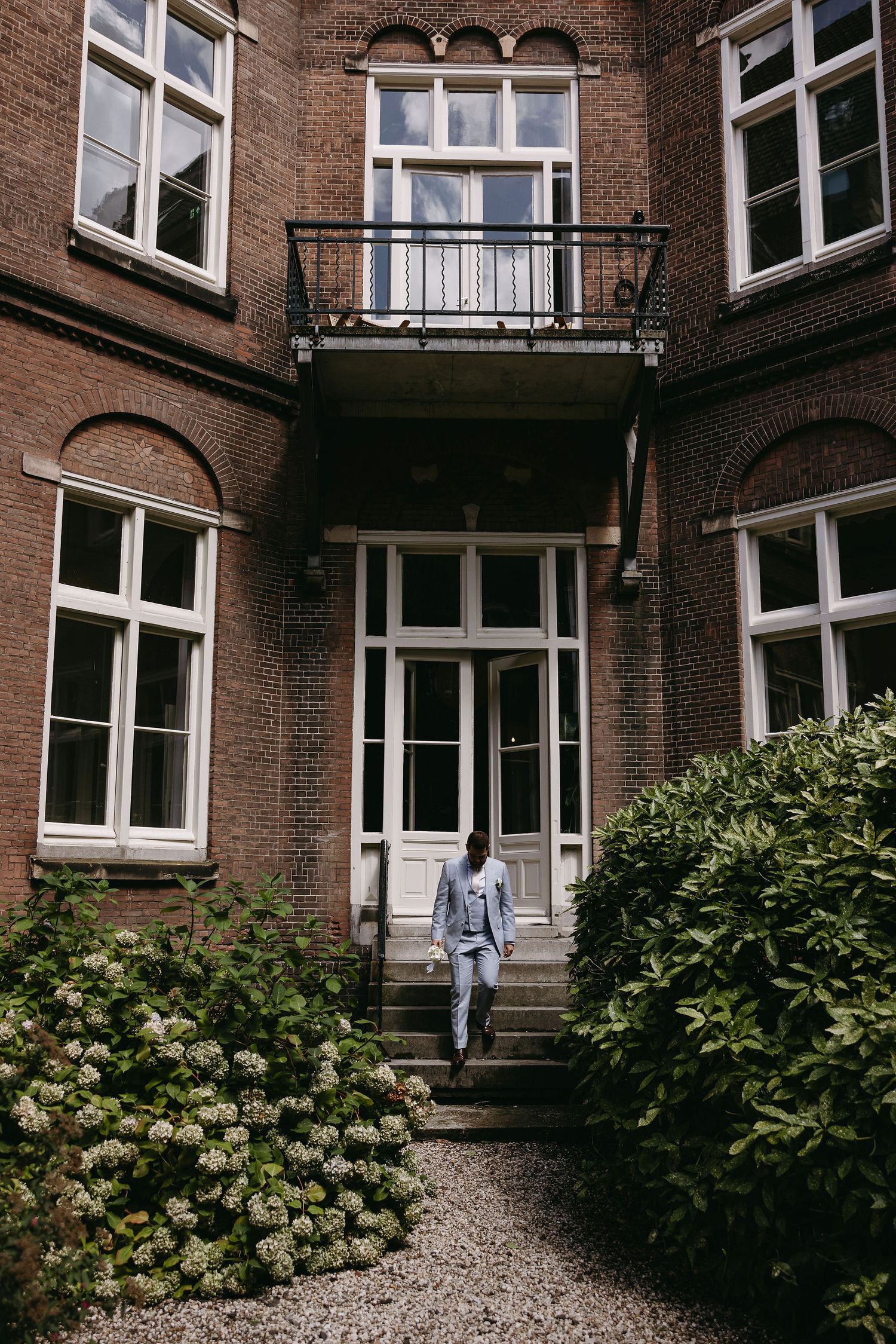 Person in blue suit ascending stairs of historic brick building with ornate balcony.