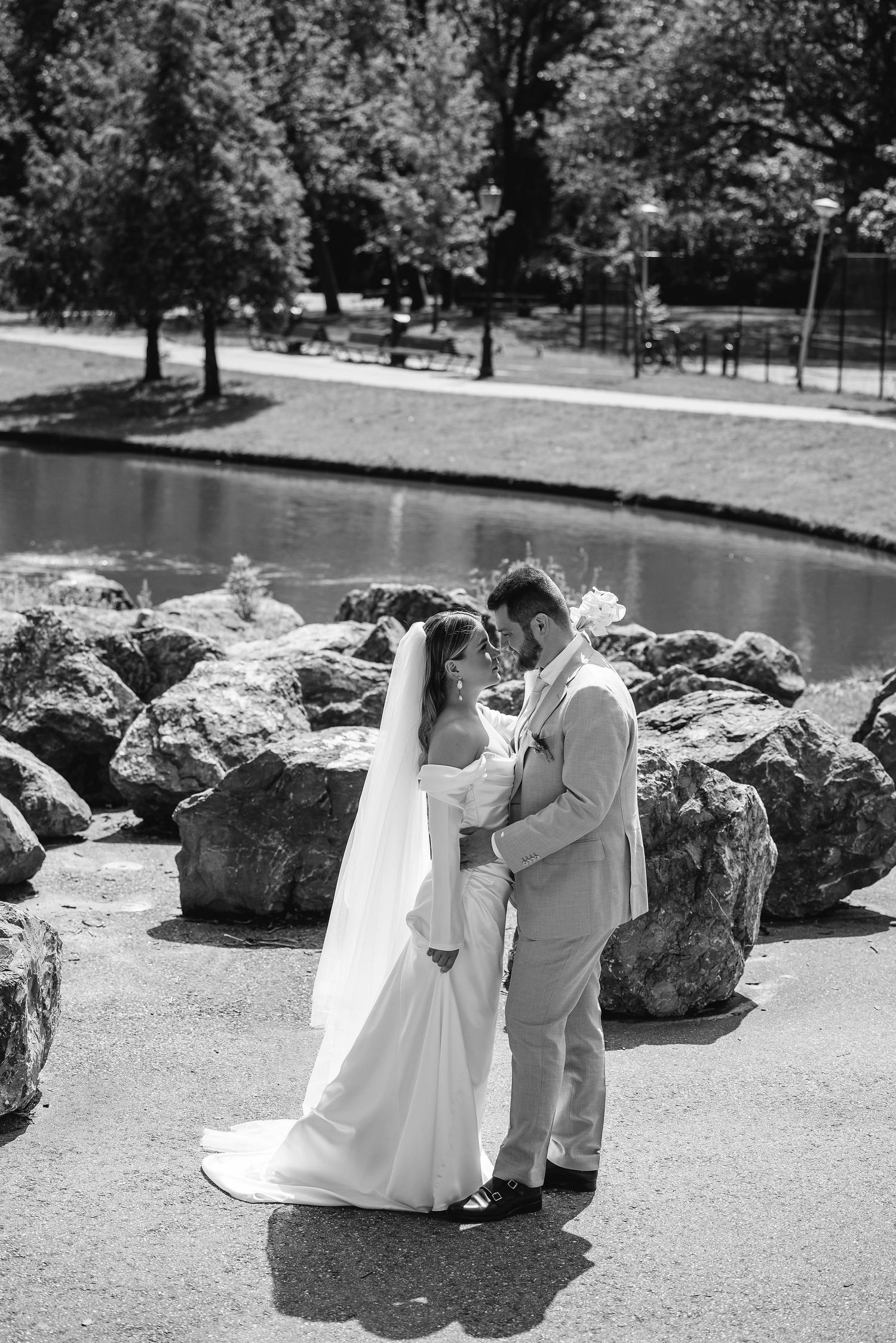 Wedding couple sharing intimate moment on rocks by lakeside in black and white photography.