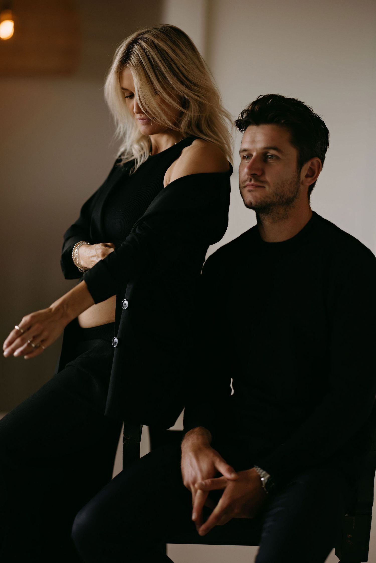 Stylish couple in matching black outfits during indoor photoshoot.