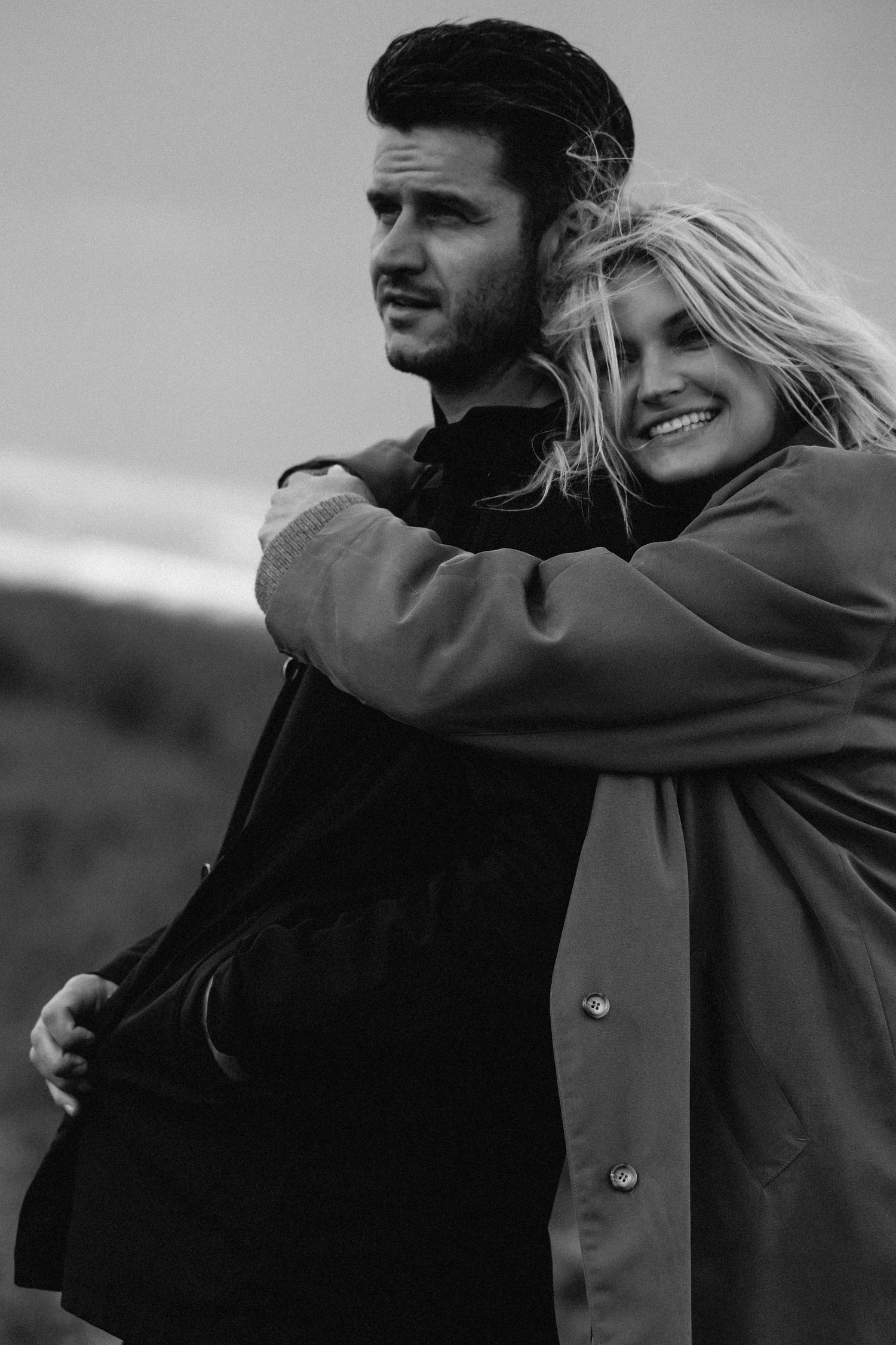 Black and white photo of couple embracing outdoors in winter coats.