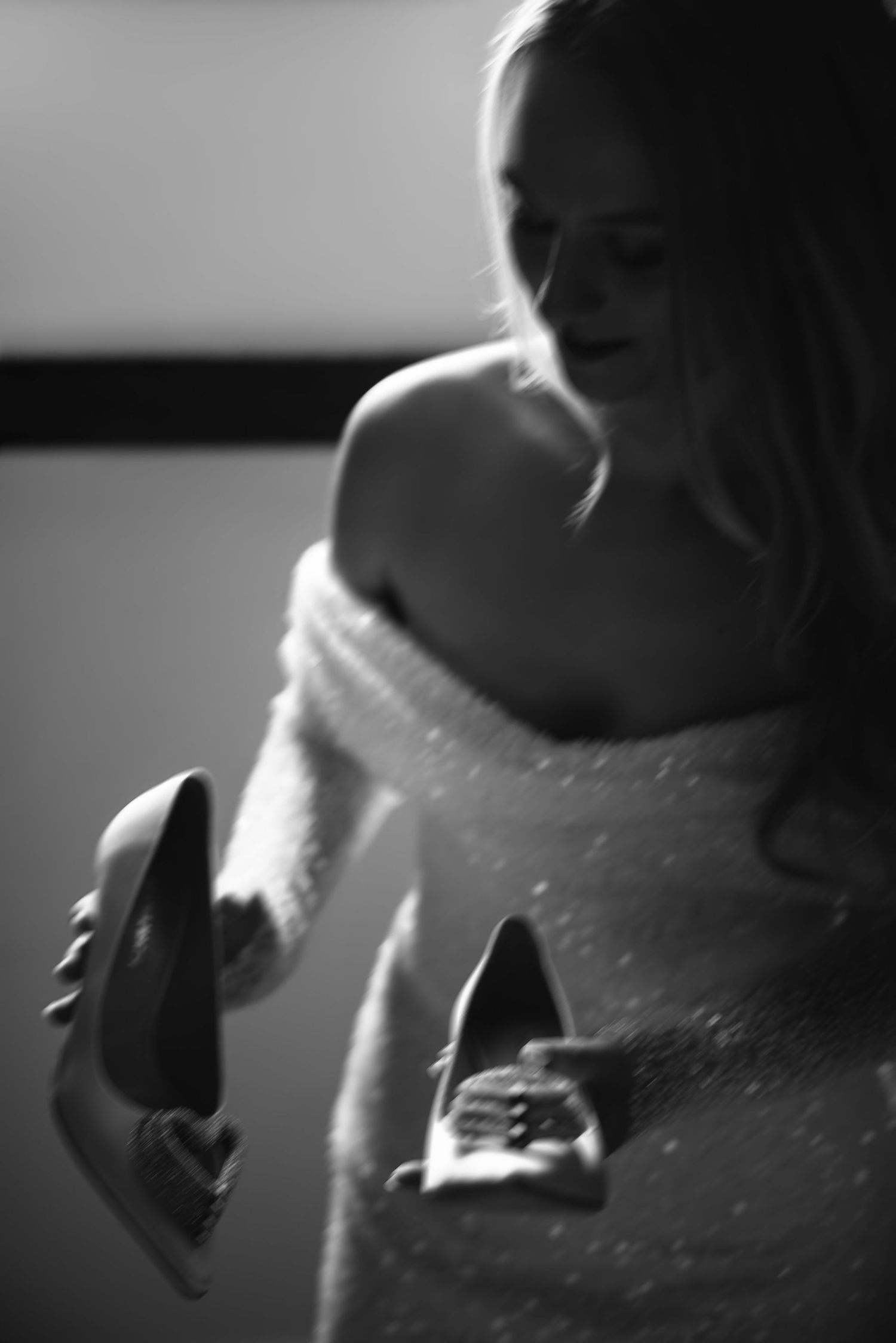 A black and white photo shows a bride holding her wedding shoes.
