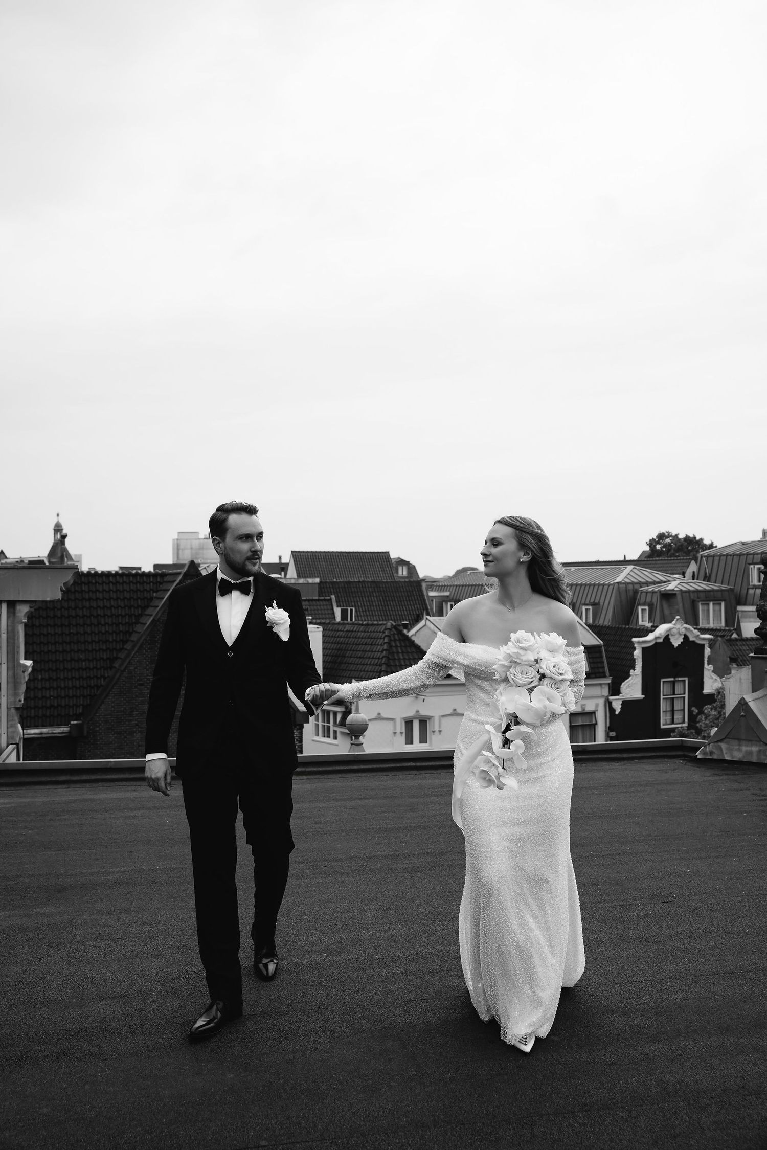 Newlyweds share playful moment while walking on rooftop.