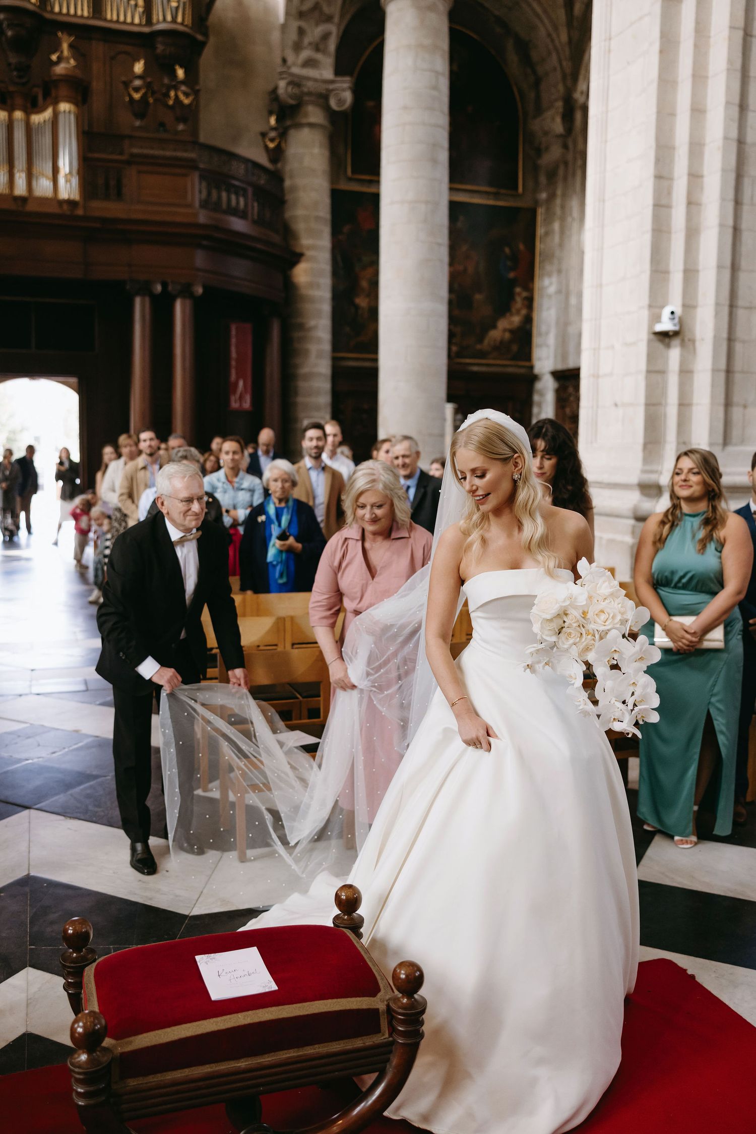 A bride in an elegant white ballgown stands in a grand church cathedral during her ceremony.