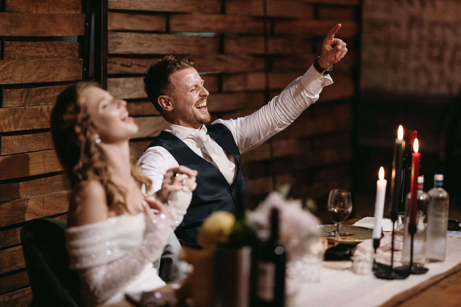 Wedding couple shares enthusiastic moment during candlelit reception dinner.