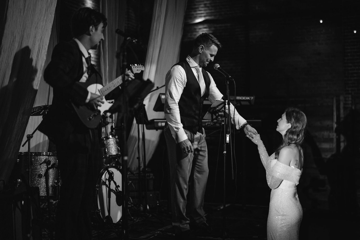 Musicians perform on stage at a wedding reception venue while interacting with wedding party guests.