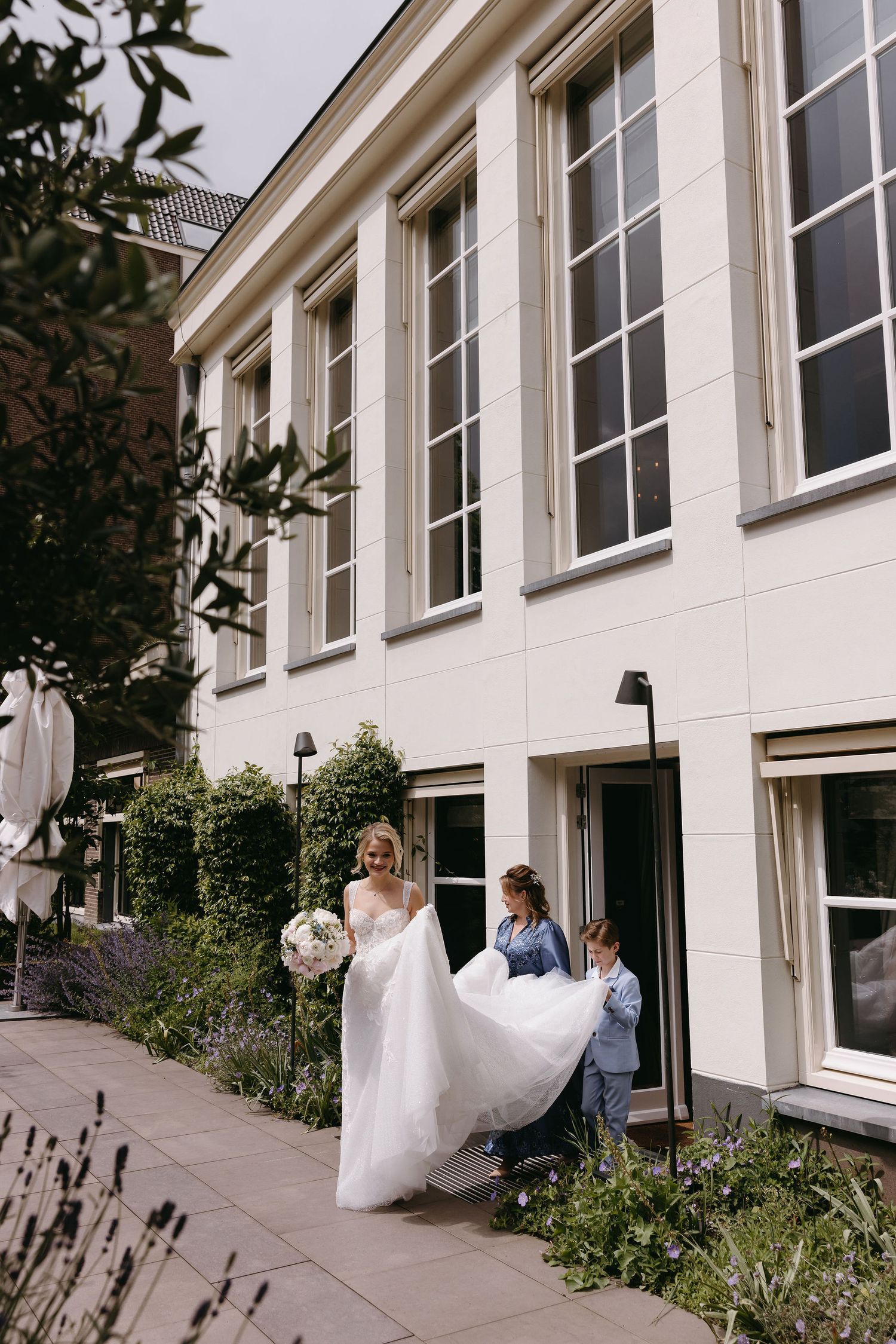 Wedding party members walking and posing along a modern building exterior with large windows.
