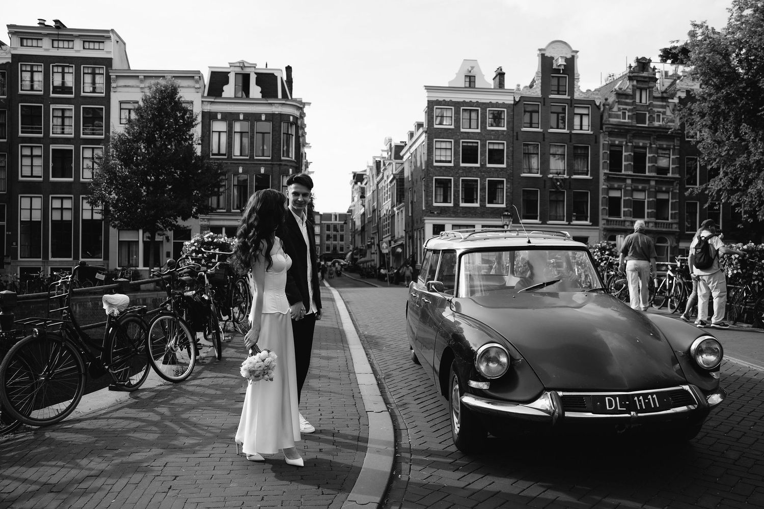 Classic Citroen DS car and bicycles line an Amsterdam canal street in a vintage black and white scene.