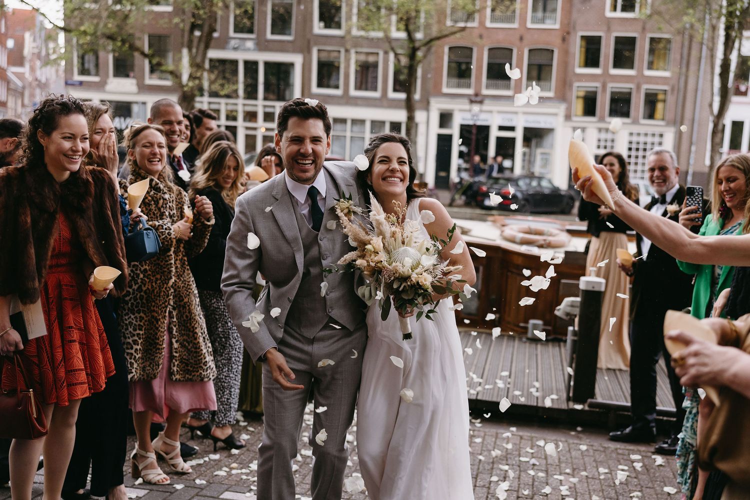 A happy couple walks through a crowd of wedding guests tossing confetti on the streets of Amsterdam.