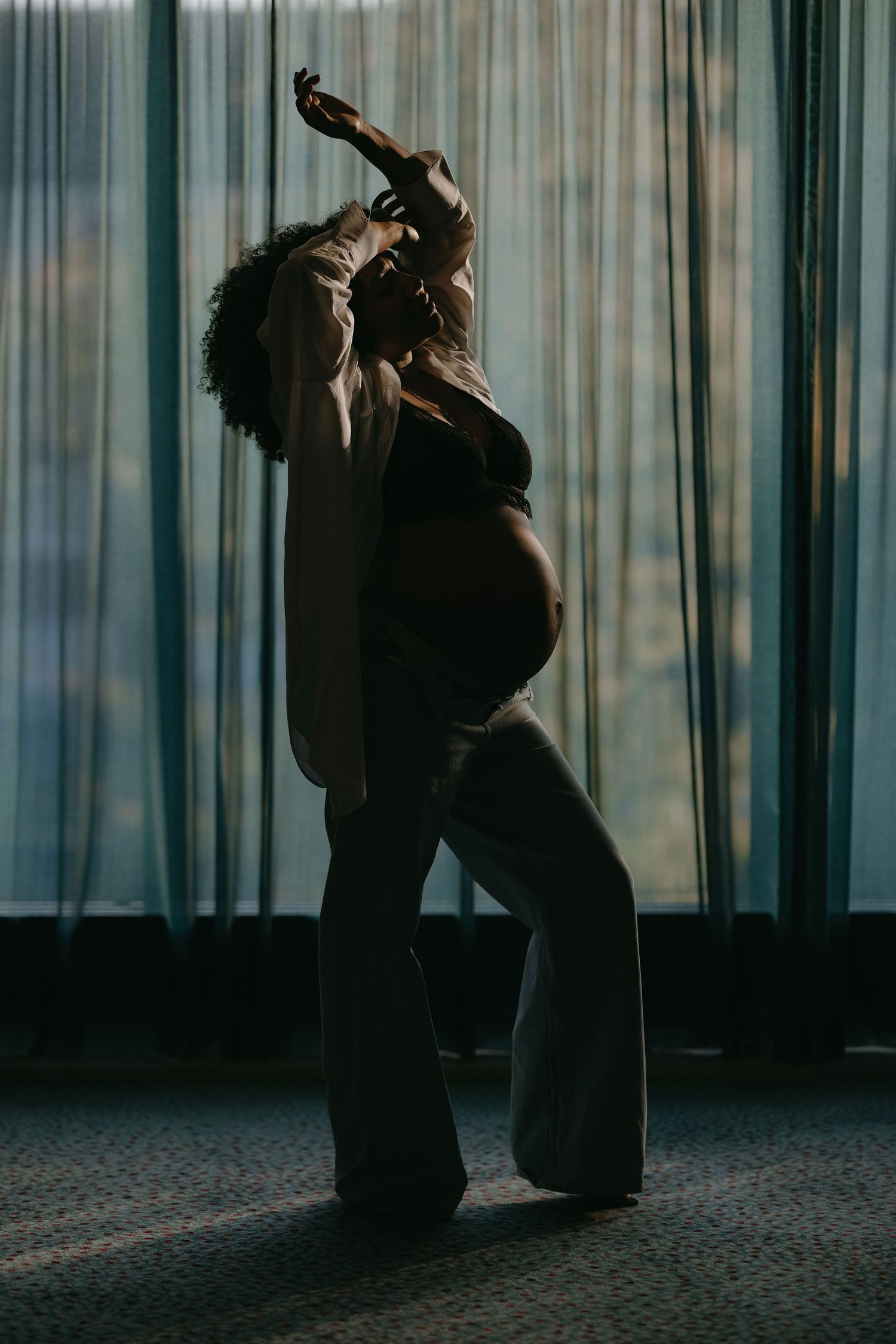A silhouetted figure in a dramatic pose against a curtained window with moody lighting.