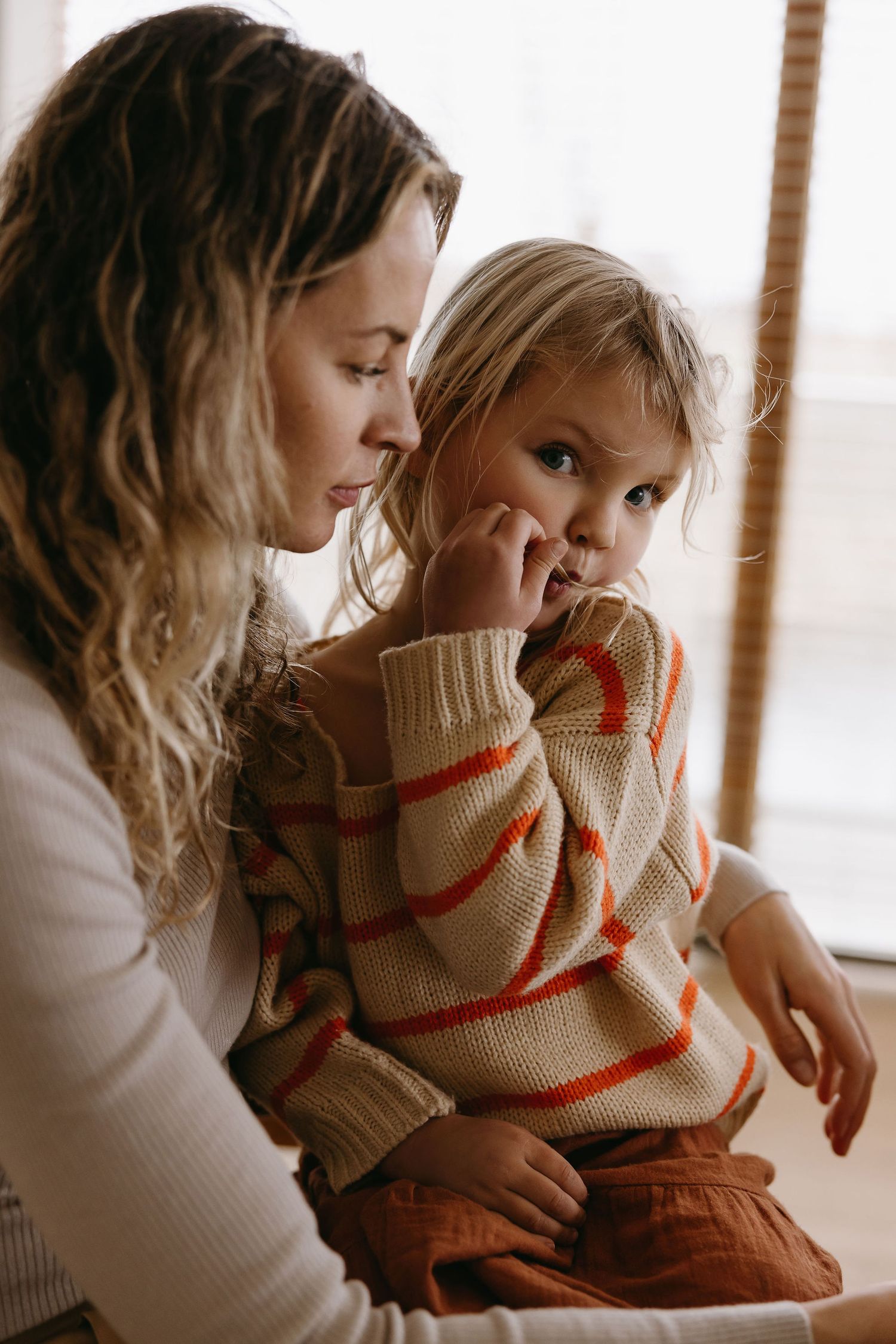 Tender family moment captured in soft window light with neutral tones.