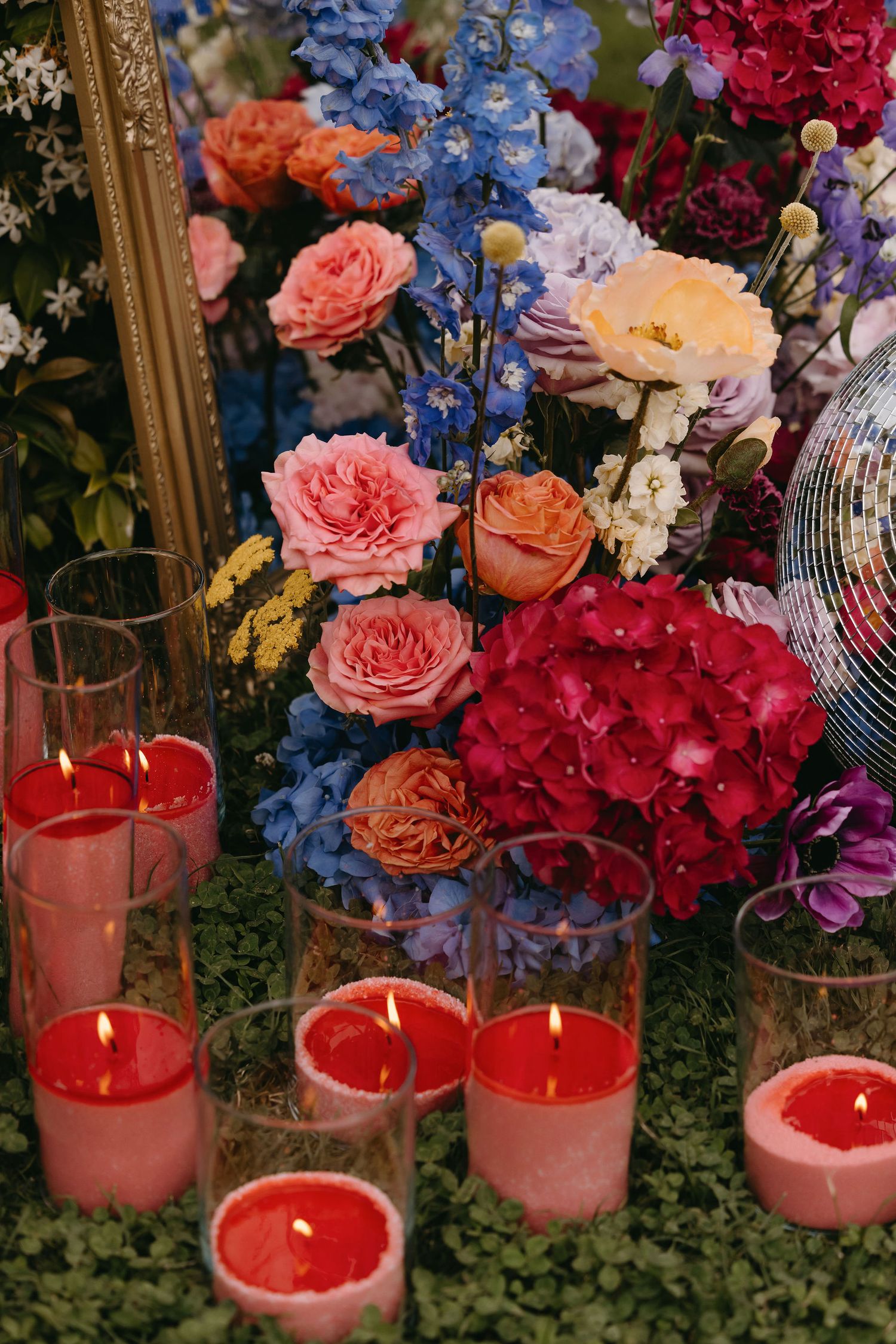 Colorful floral arrangement with pink roses, blue delphinium, and red candles creating an elegant wedding centerpiece.