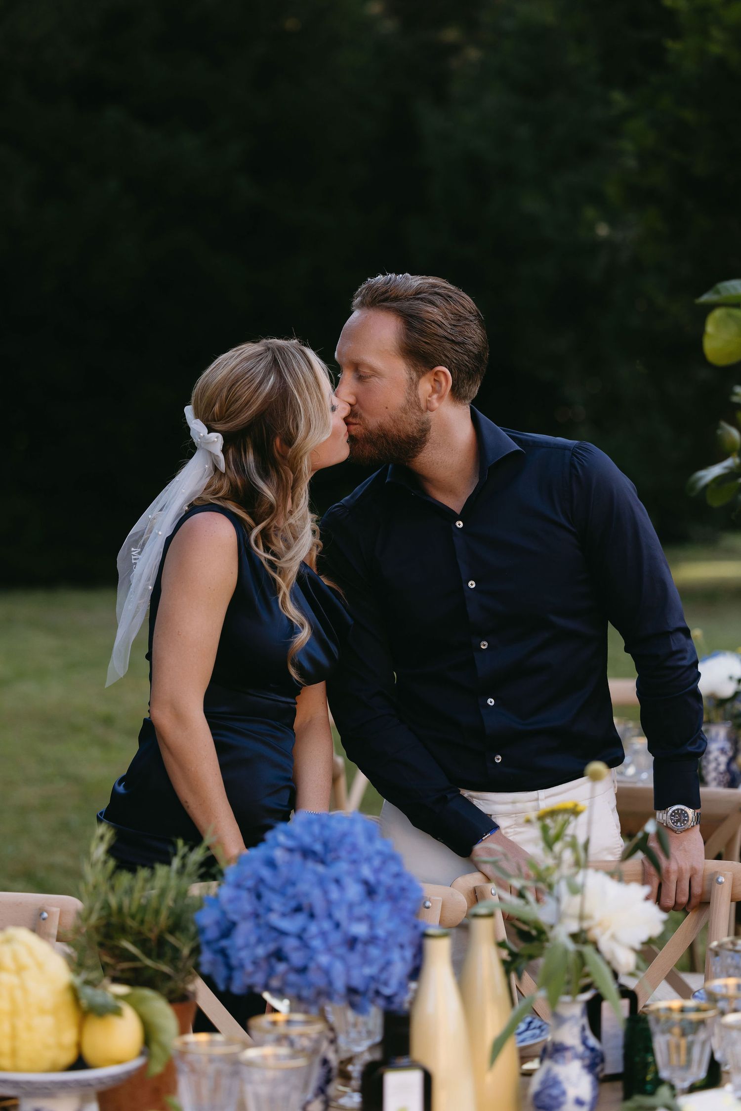 Intimate outdoor dining scene with blue hydrangeas and wine bottles on rustic table.