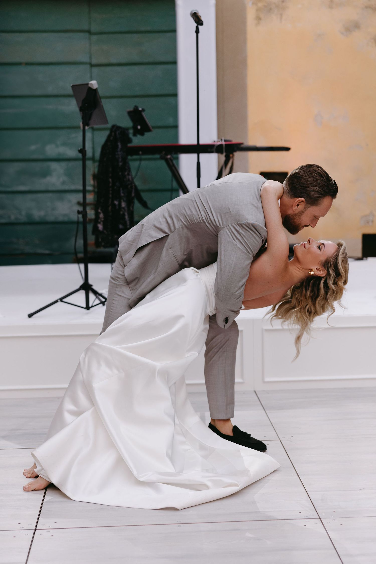 A romantic dip dance pose on a light colored dance floor at a wedding celebration.
