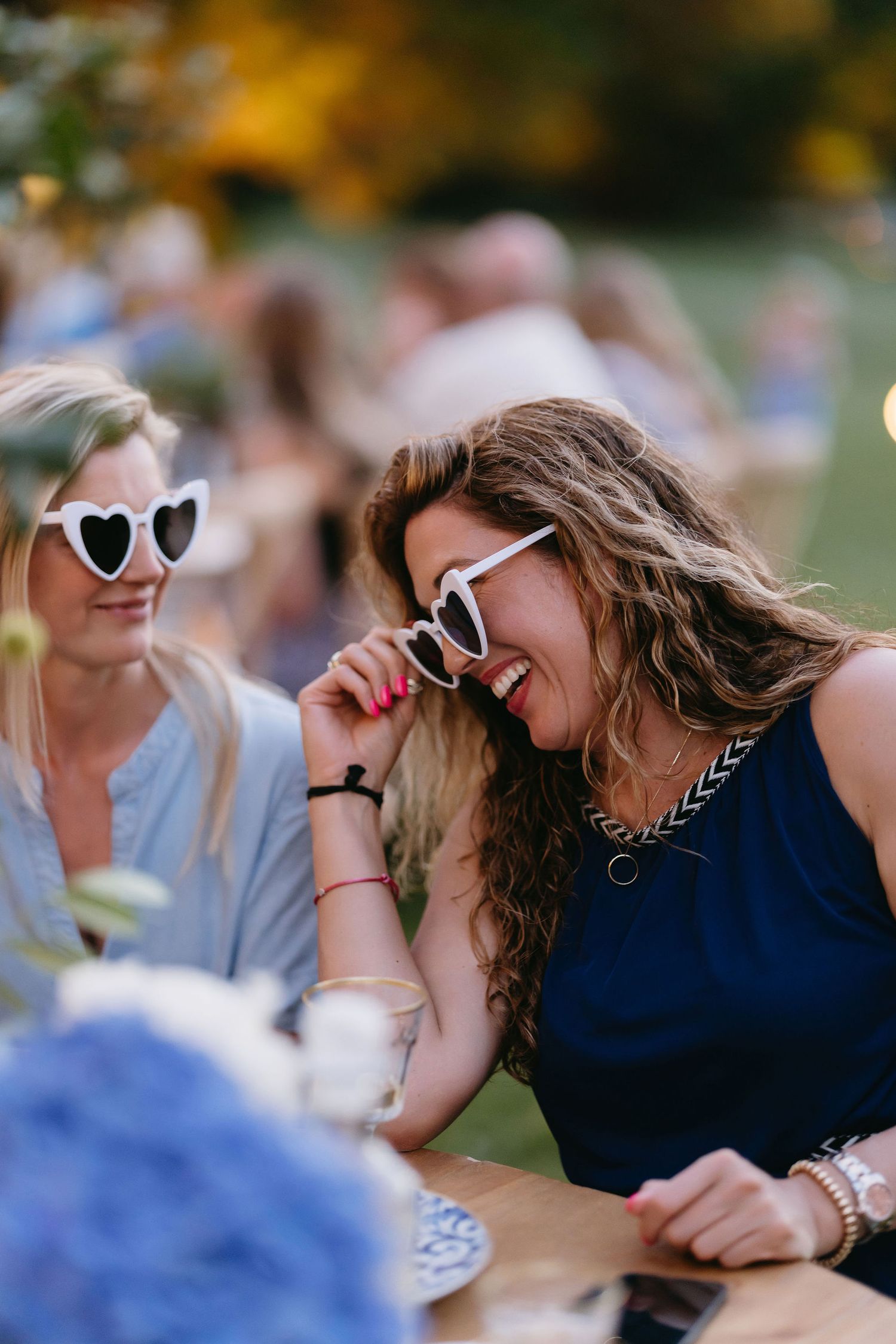 Joyful moment shared between friends wearing sunglasses at an outdoor gathering.