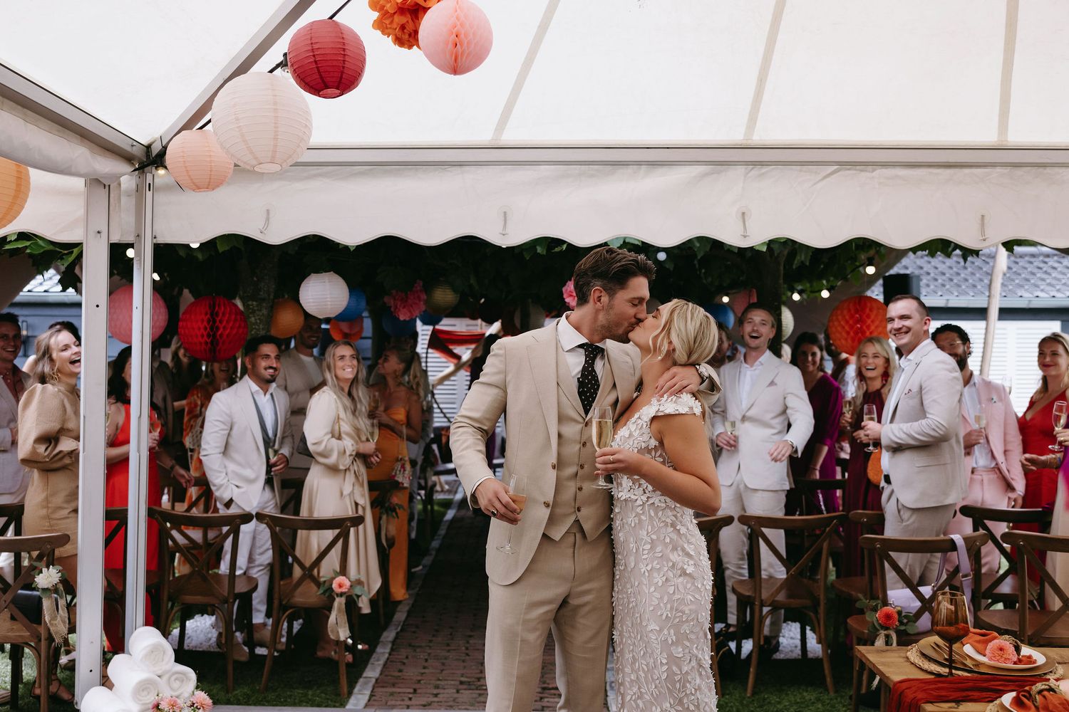 Couple dancing under white tent with festive red lanterns at wedding reception.