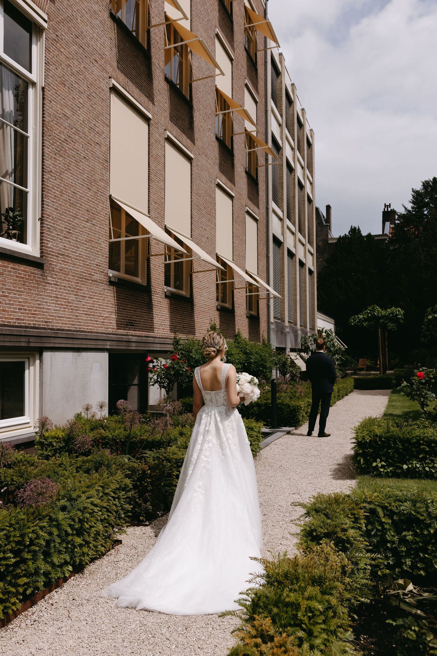 White wedding dress photographed against modern apartment building exterior with landscaped path.