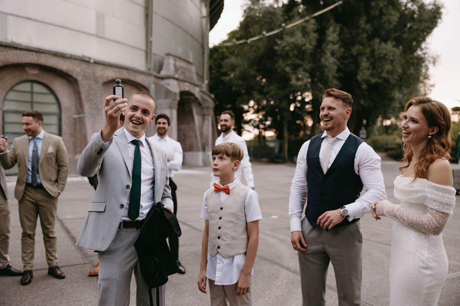 Wedding party lined up in formal attire against a white building exterior.