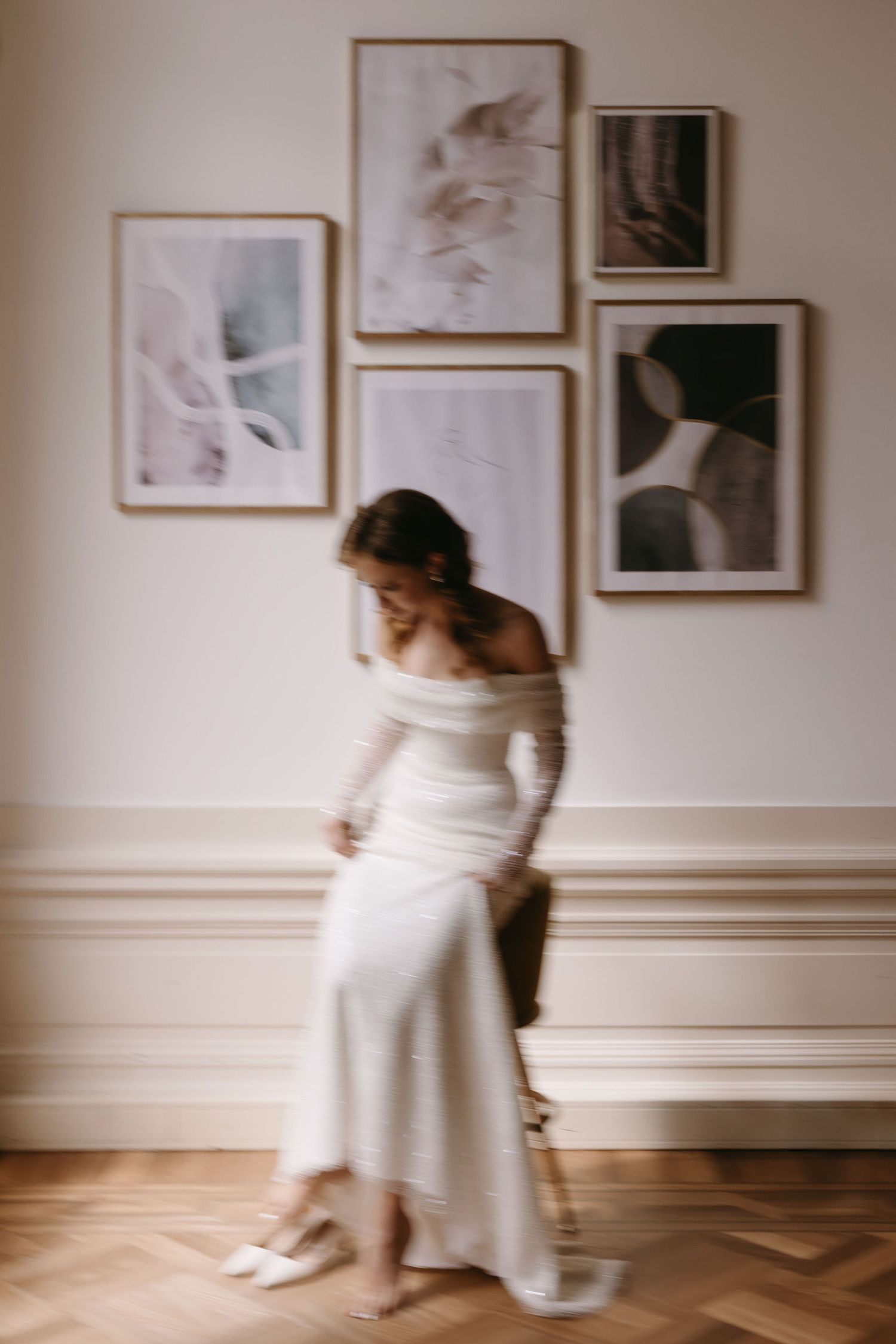 Artistic motion blur portrait of a bride in an off-shoulder wedding dress against a gallery wall.