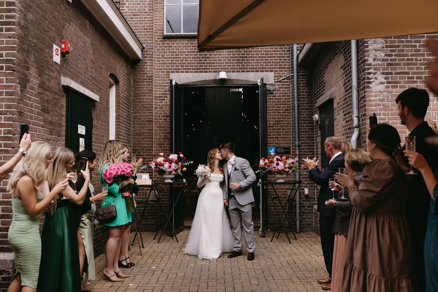 Wedding couple celebrating with guests outside a brick building venue.
