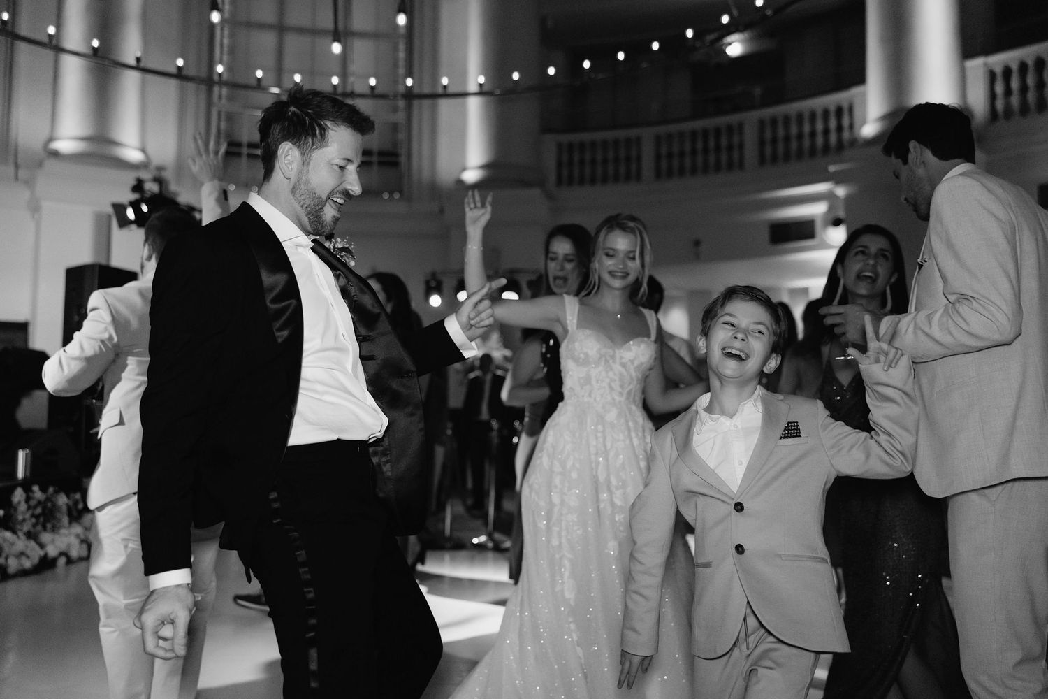 Black and white photographs showing joyful dancing and celebration at an indoor wedding reception.