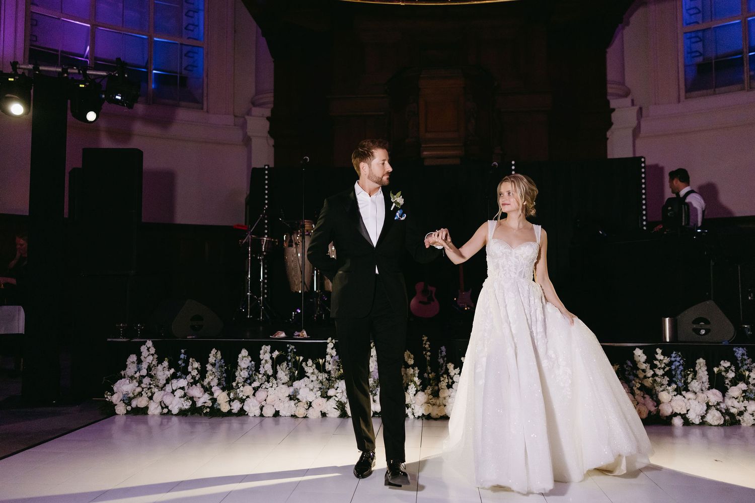 A couple shares their first dance on a ballroom floor decorated with white flowers.