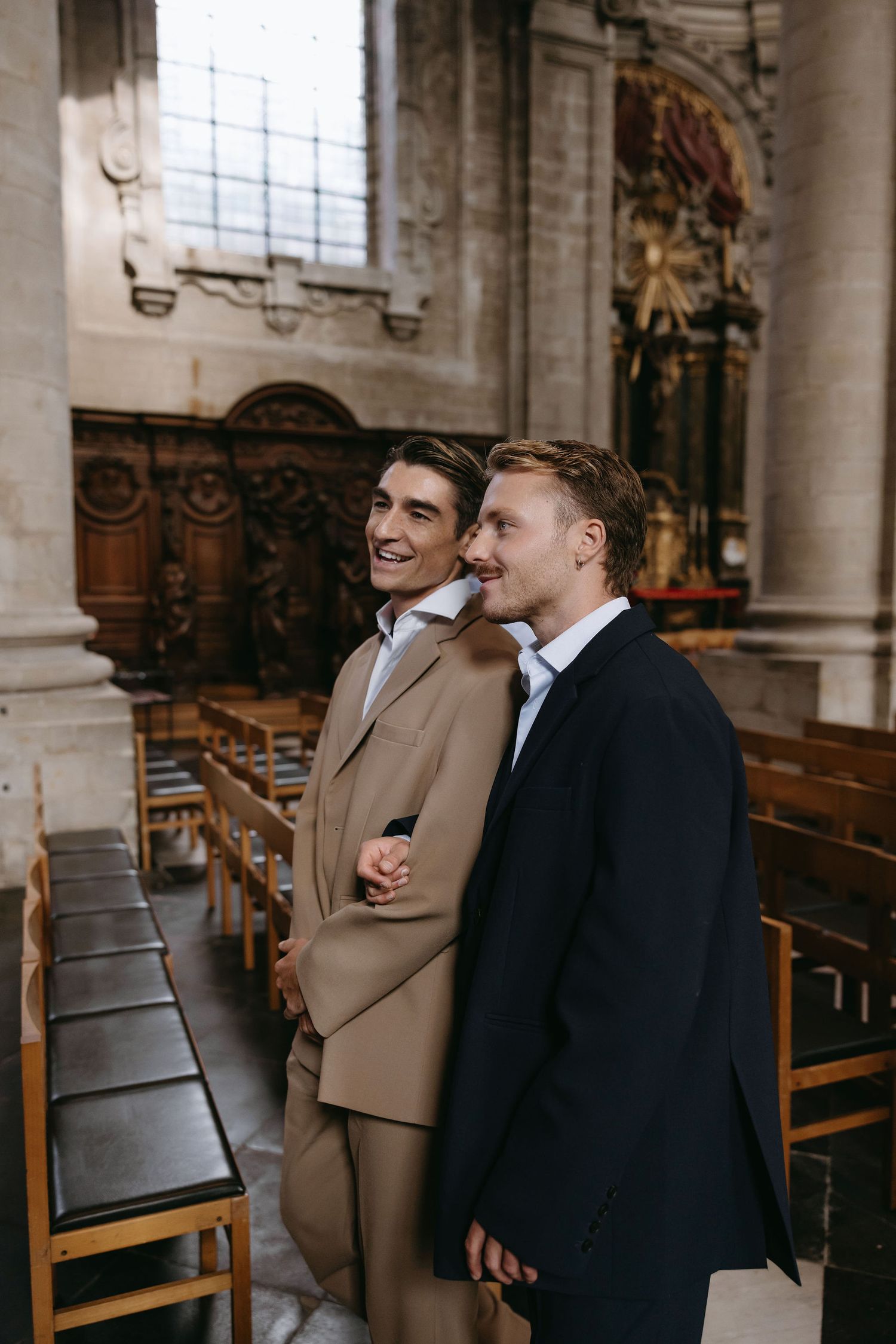 Two guests in suits standing in a historic church interior with ornate architecture.