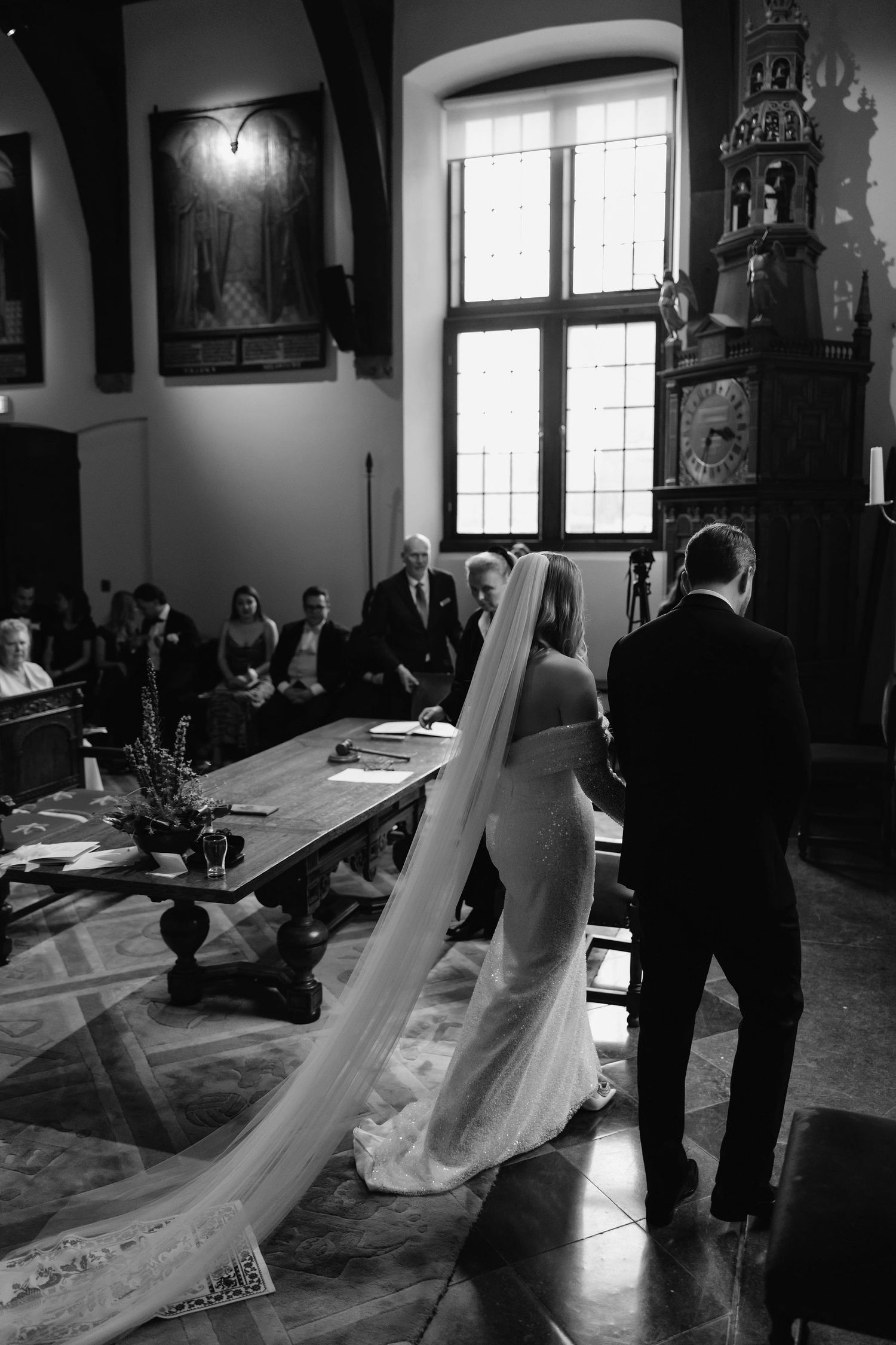 Black and white ceremony photo in historic venue with dramatic veil and architectural details.