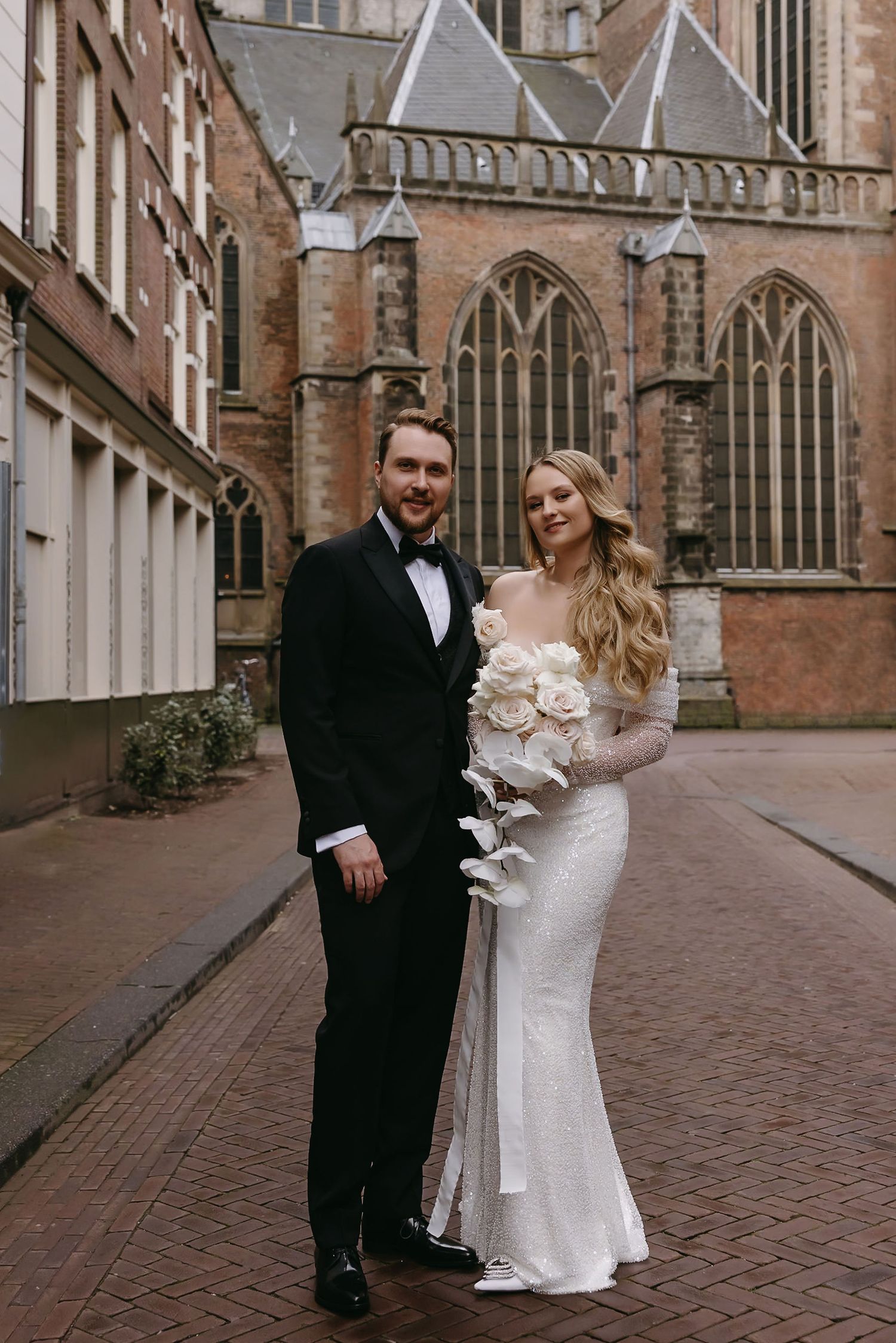 Wedding couple posing outside historic church with gothic architecture and brick details.