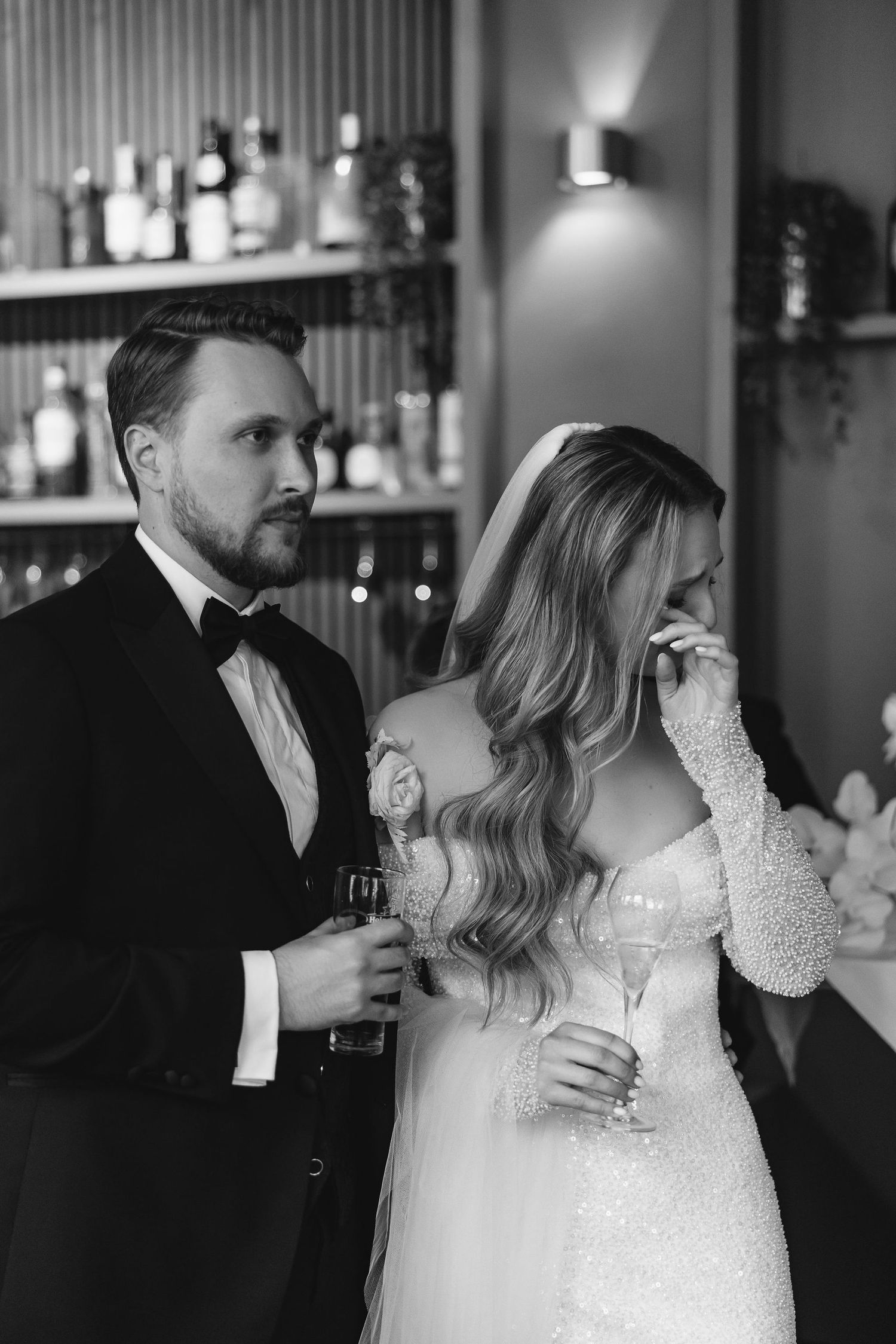 Elegant wedding couple sharing an intimate moment at a bar with champagne glasses in black and white.