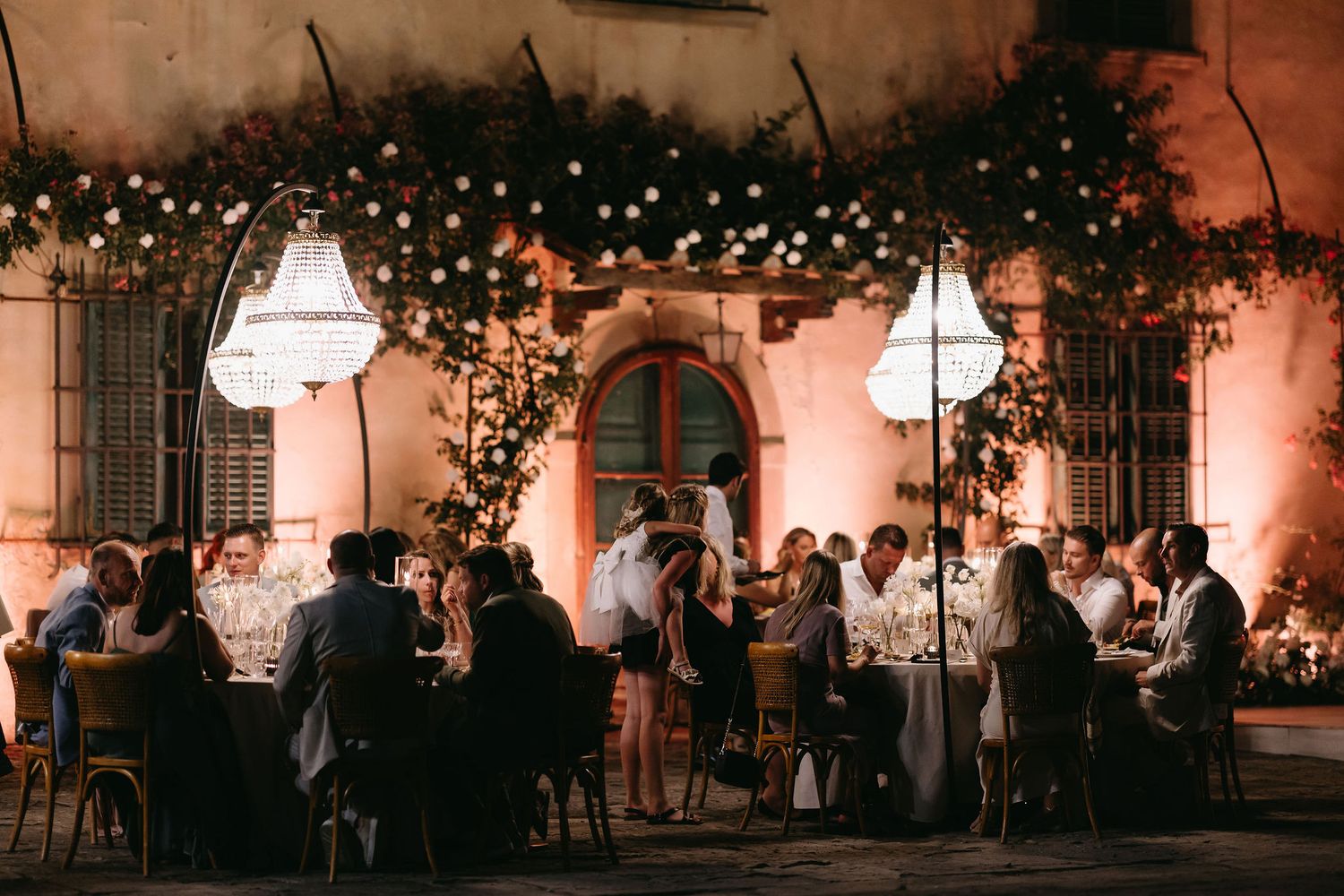 Outdoor wedding reception at dusk with string lights and hanging lanterns creating a romantic atmosphere.