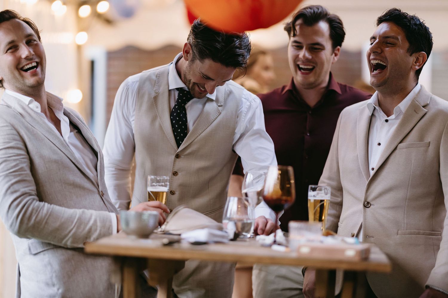 Wedding guests in light suits laughing and enjoying drinks at reception.