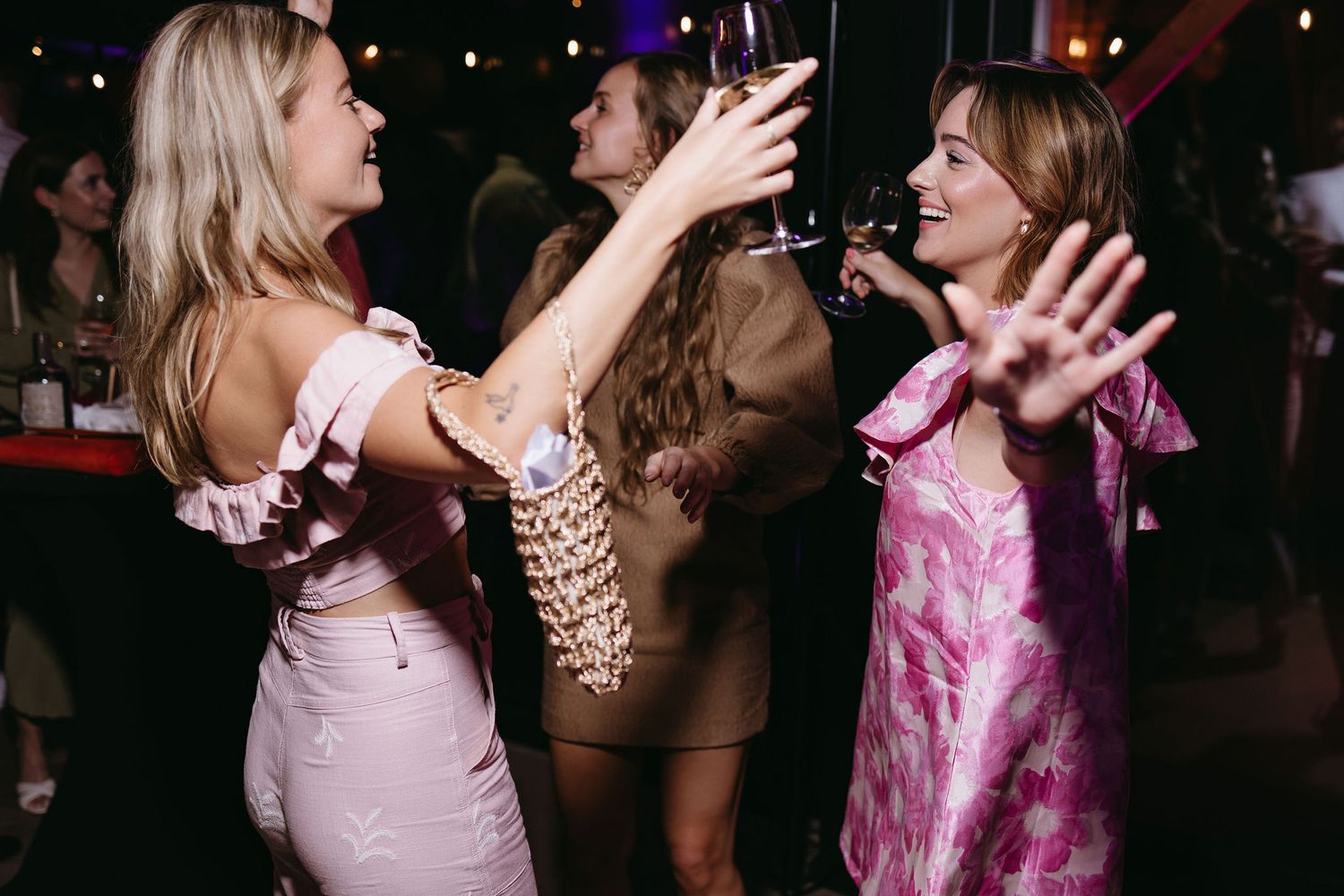 Party guests in pink dresses dance and celebrate at a lively event.