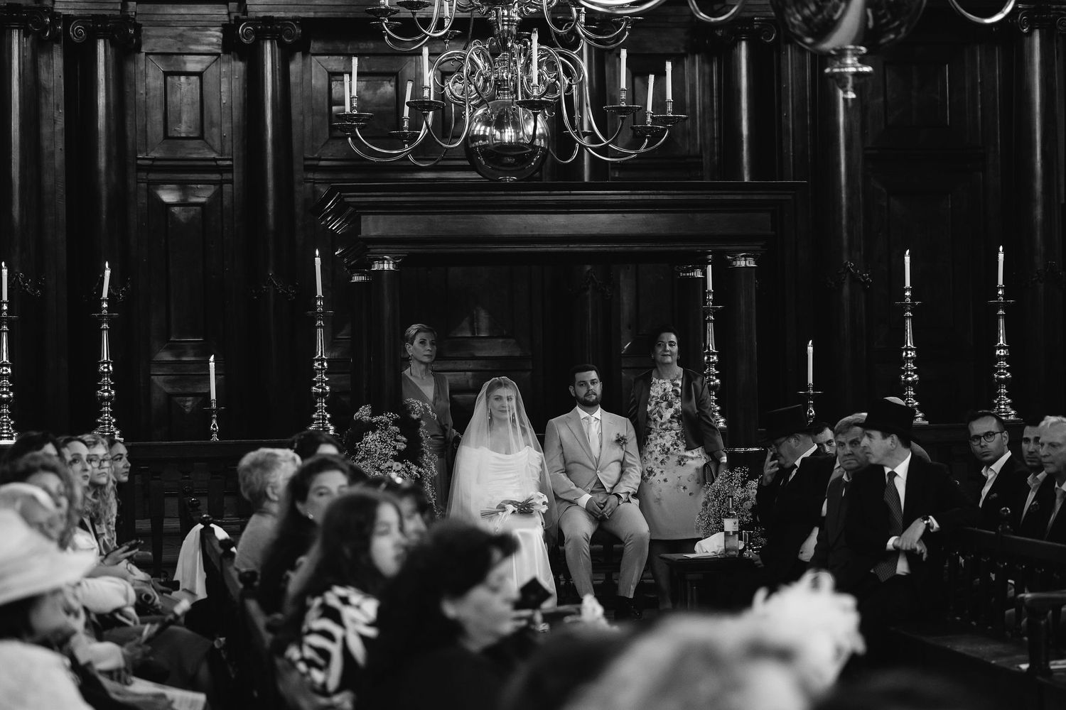 Dark reception venue with chandeliers and guests seated at formal dining tables.