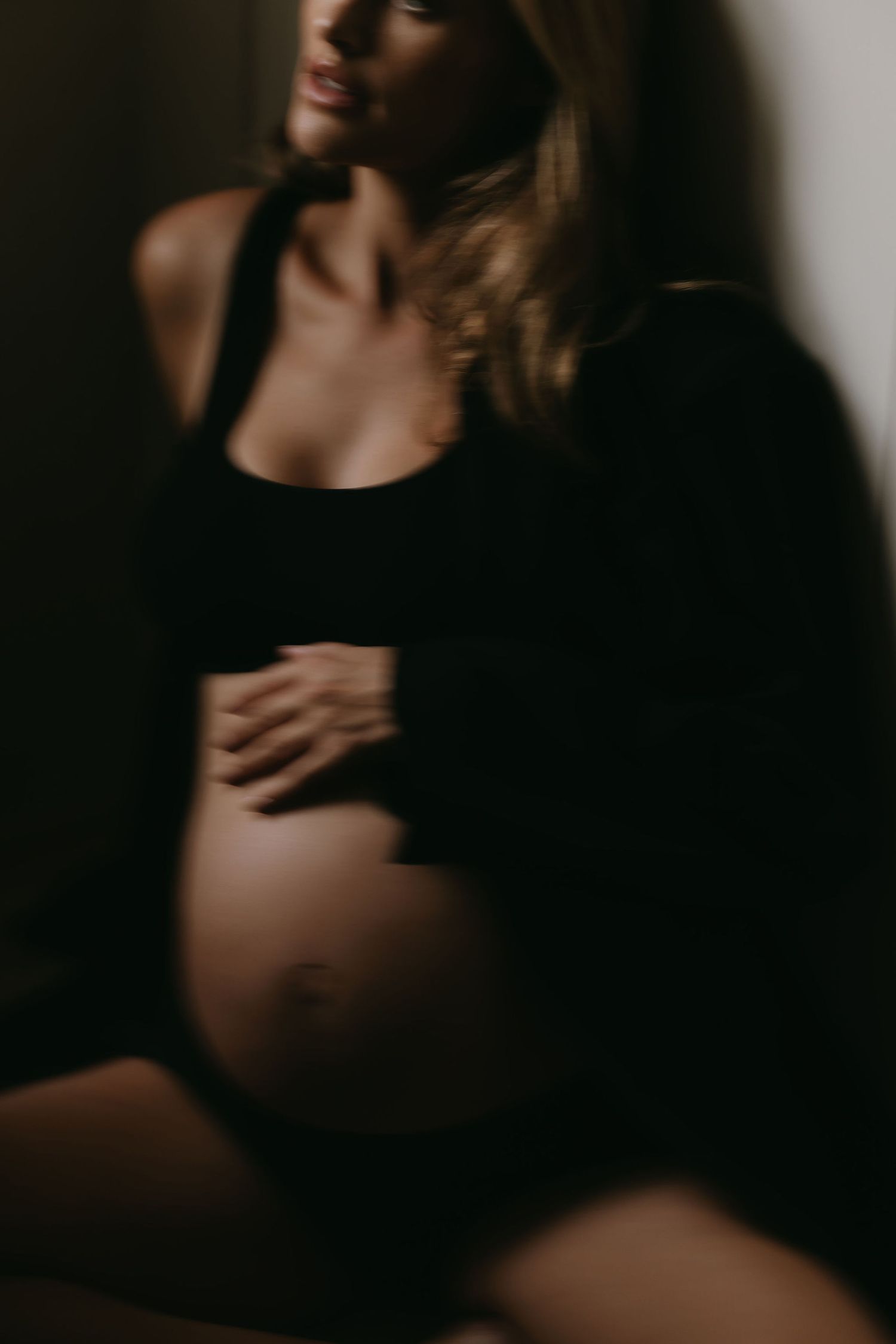 Moody maternity portrait in dark lighting showing pregnant belly.