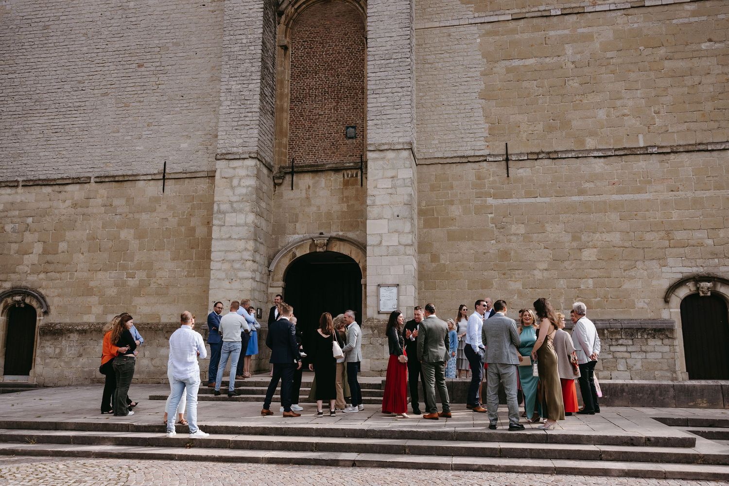 Group of wedding guests gathered outside a historic stone church building.