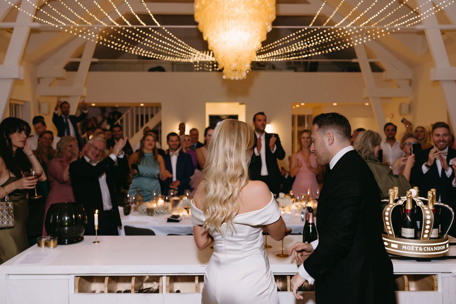 Wedding celebration in an elegant venue with string lights and chandelier.