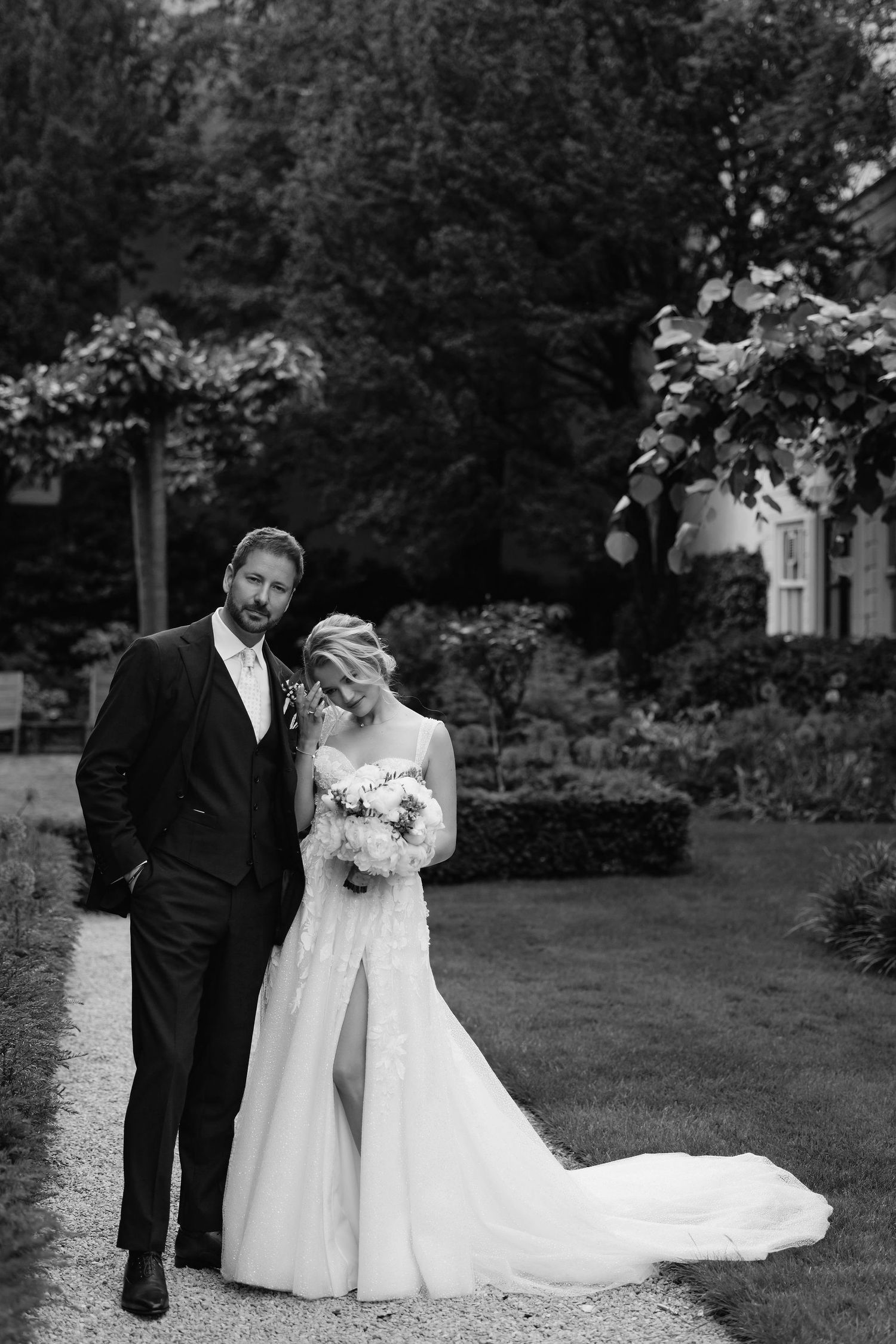 A wedding couple poses for a portrait in a lush garden setting.
