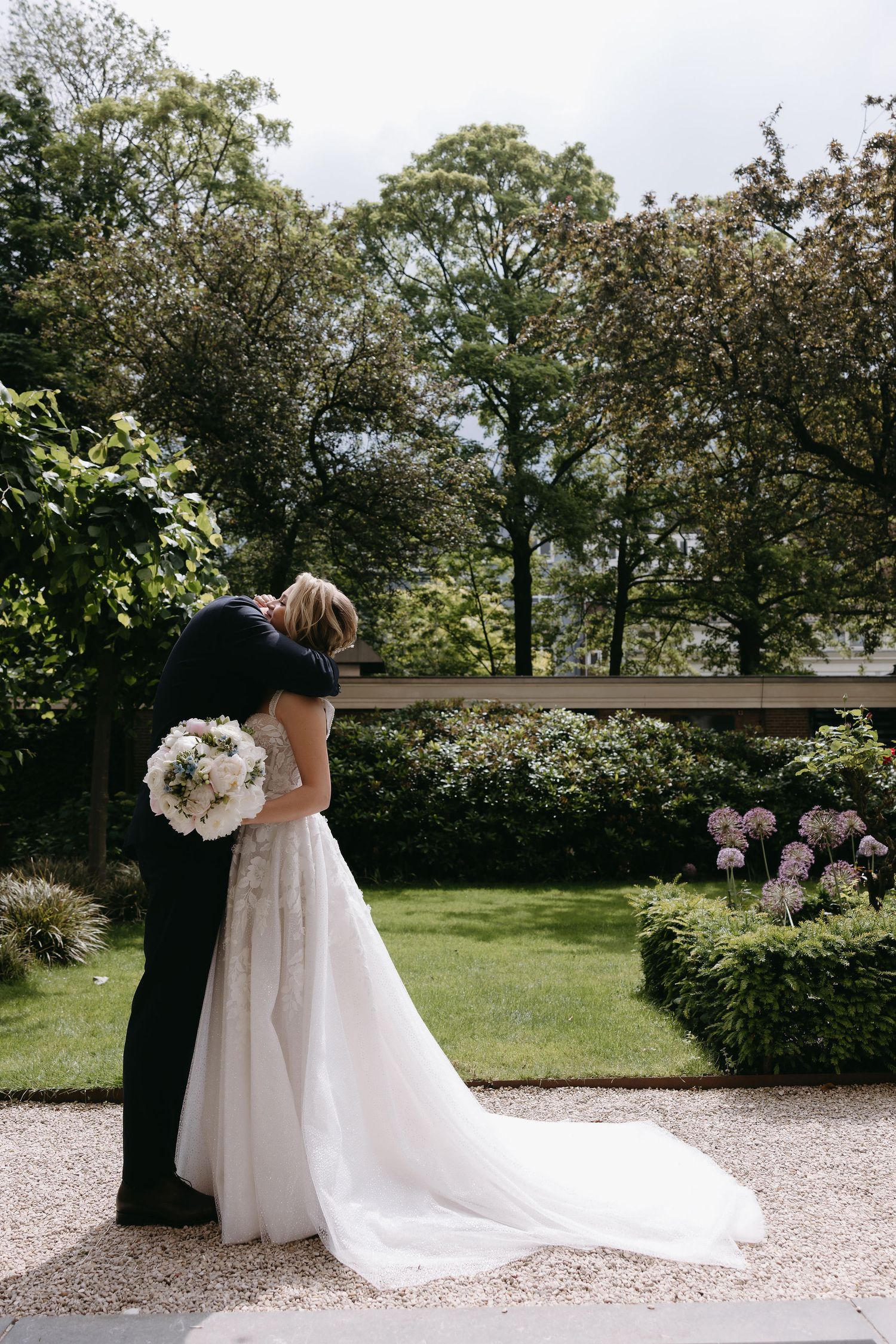 A couple shares an intimate moment in a garden setting with white floral arrangements.