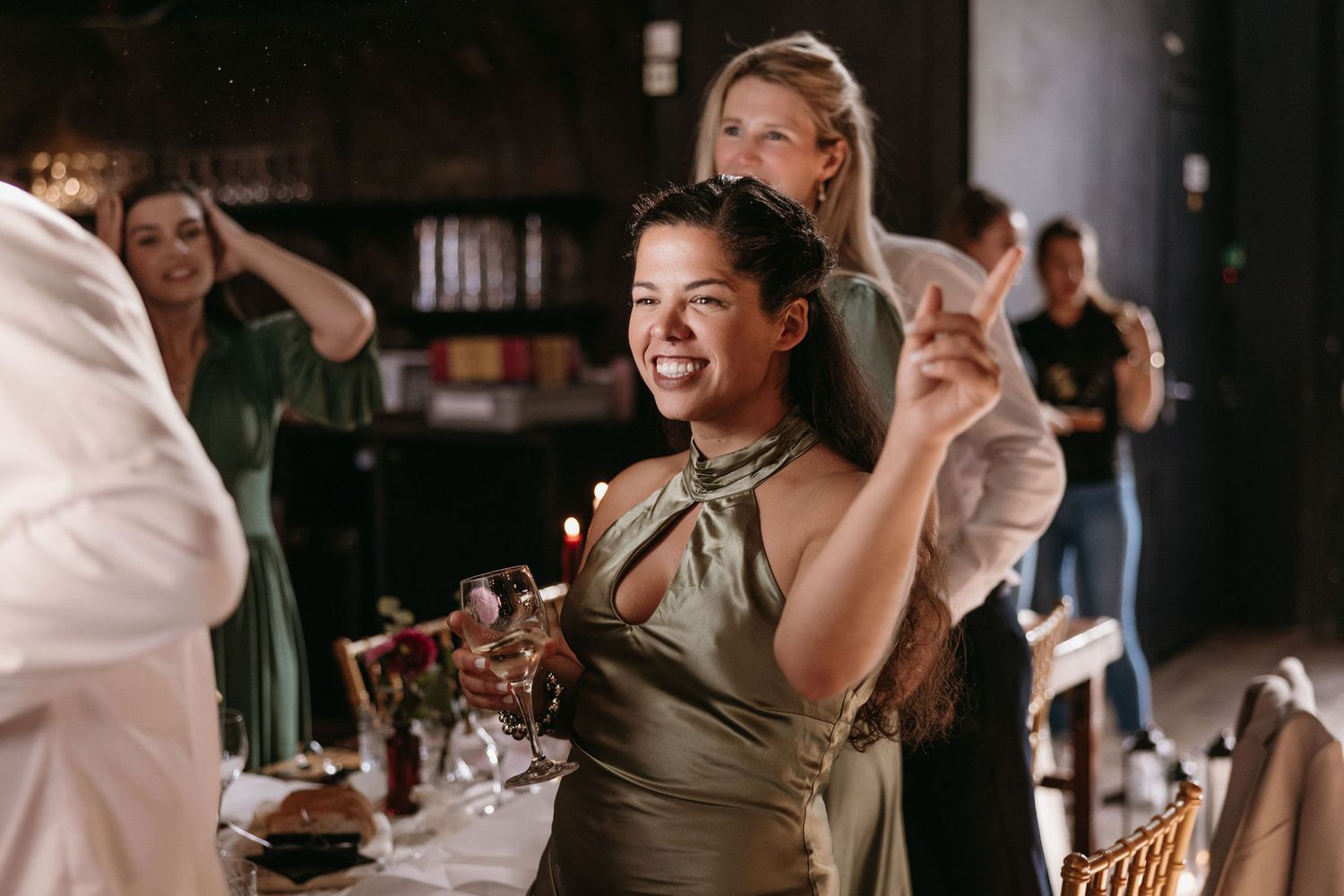 Wedding reception guests enjoy drinks and conversation at tables in a rustic venue setting.
