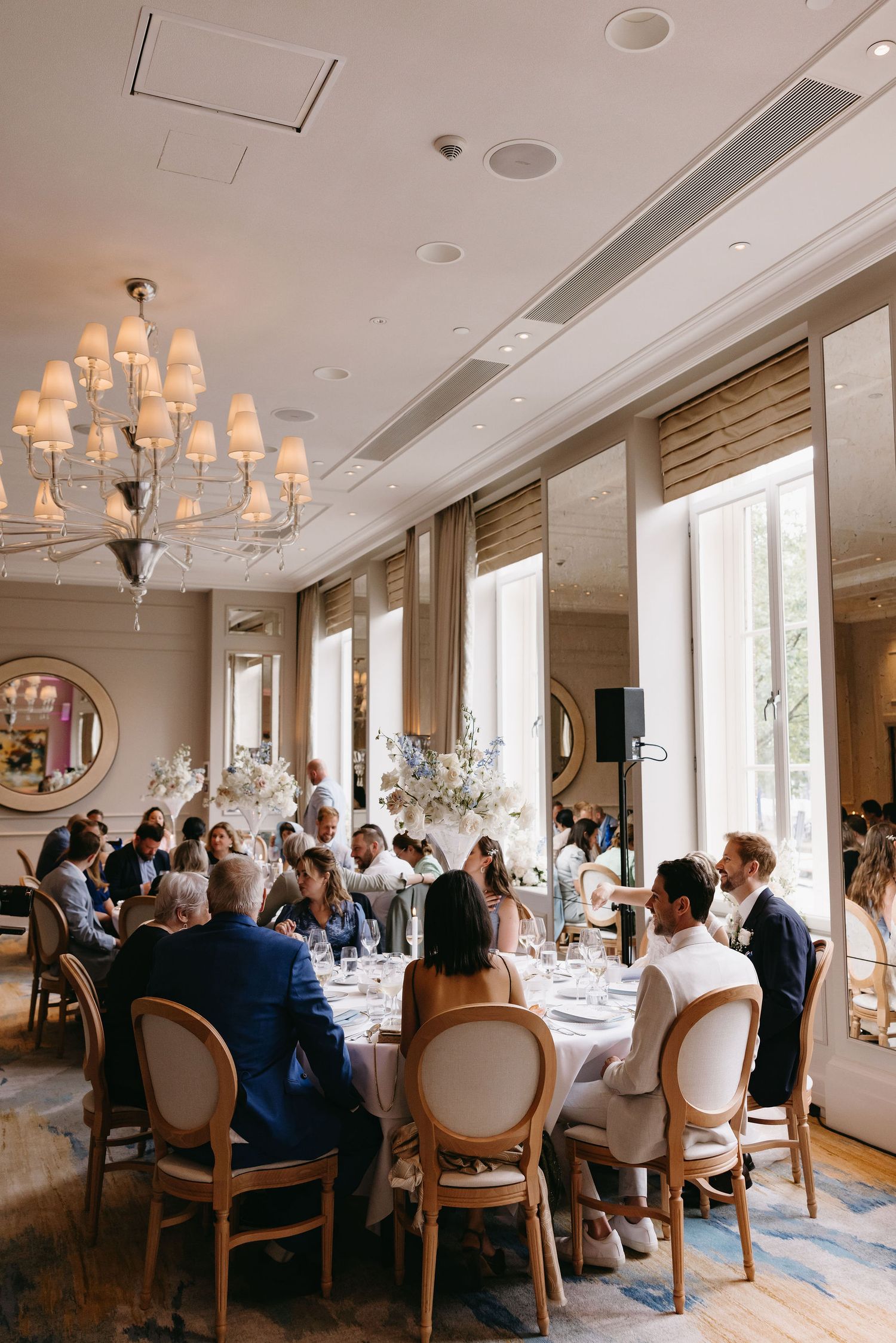 Elegant wedding reception setup with chandelier and round tables in a bright, airy room.