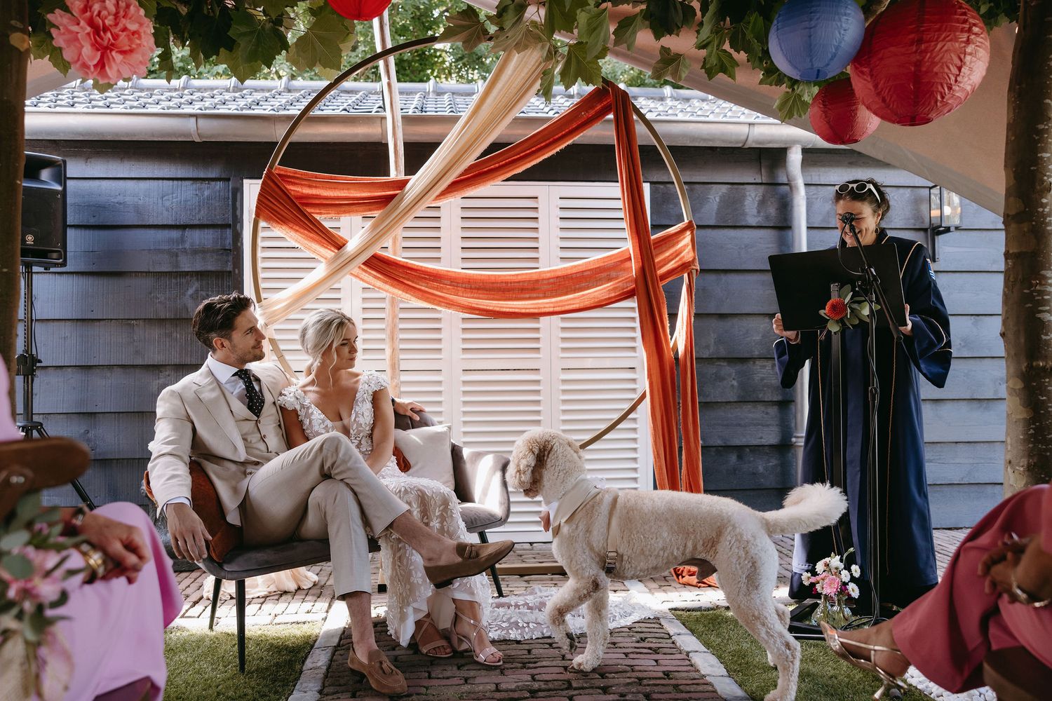Outdoor wedding ceremony setup with white chairs, orange draping, and a dog walking through.