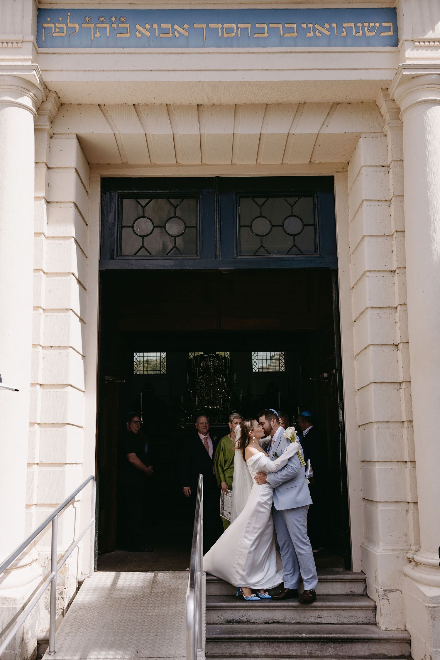 Wedding ceremony at historic synagogue entrance with Hebrew text inscription above.