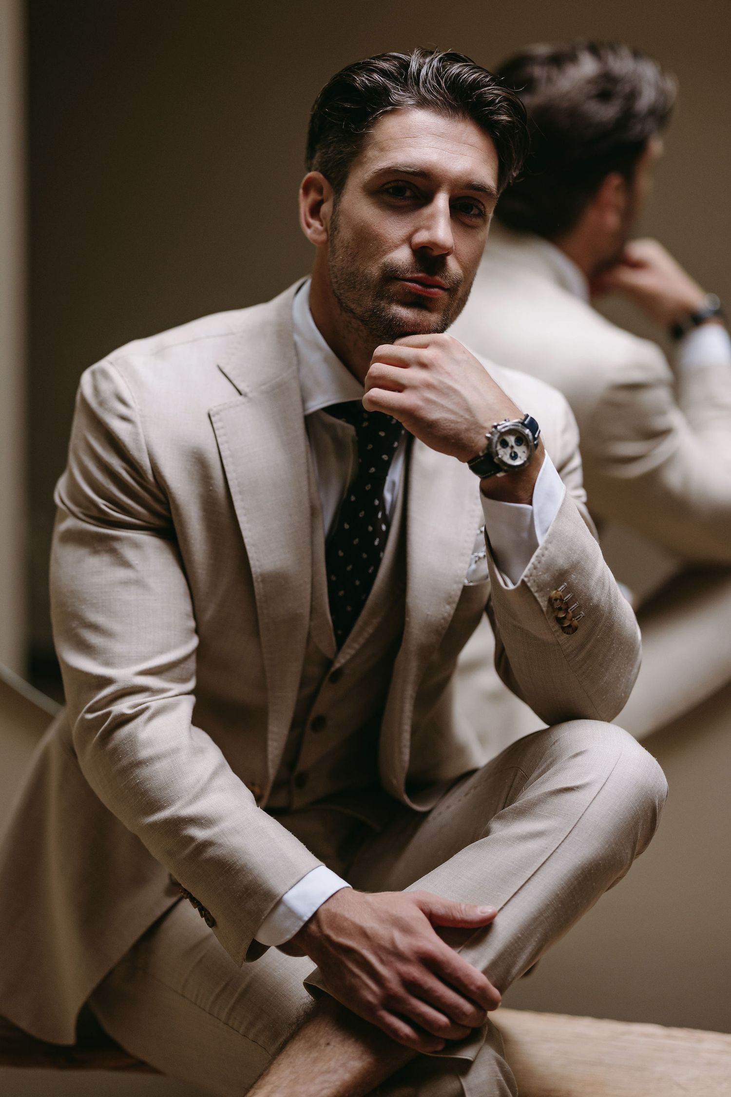 Groom in beige suit posing thoughtfully in artistic portrait series.