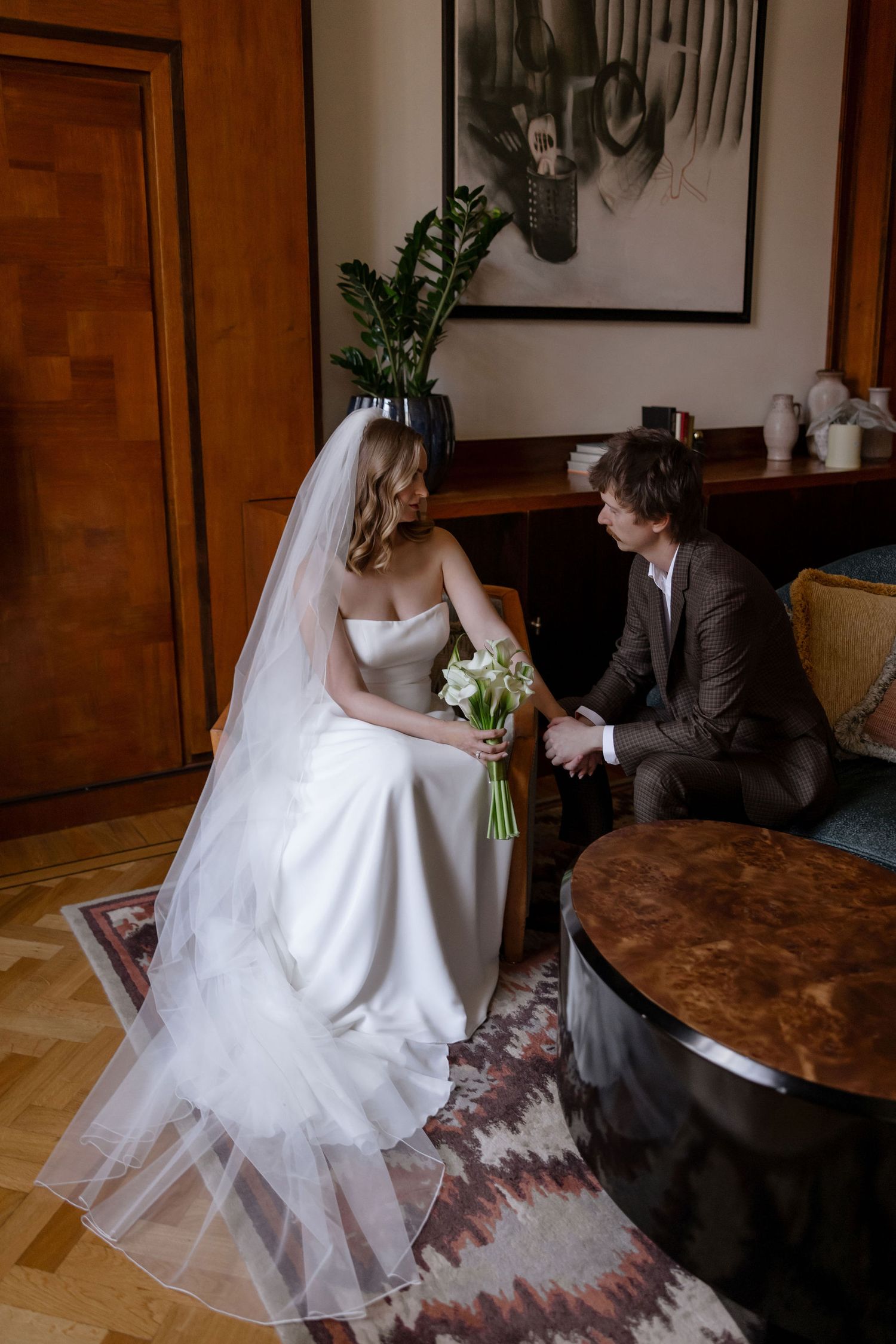 A tender moment between a bride and groom seated in an elegant indoor setting with vintage furniture.