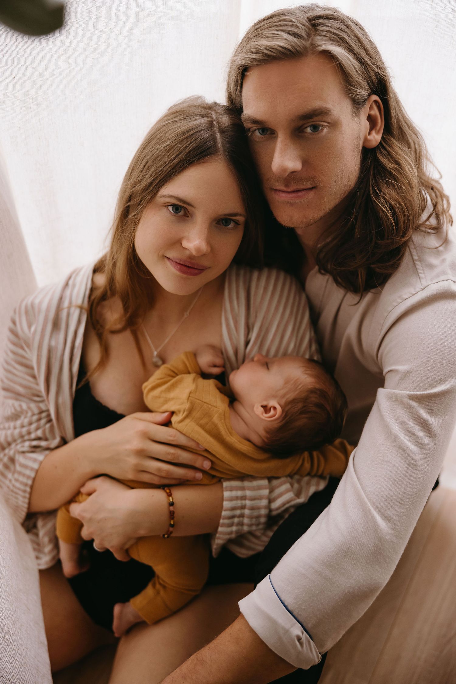 A serene family moment as parents cuddle with their baby in a soft, natural light setting.