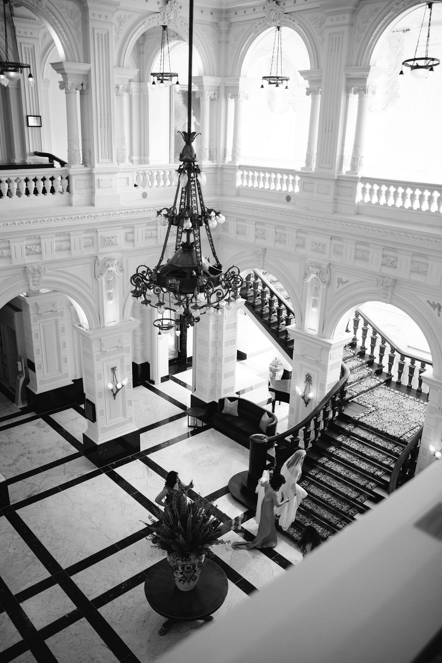 A series of four black and white photos showing an elegant grand staircase in a classical building interior with chandeliers.