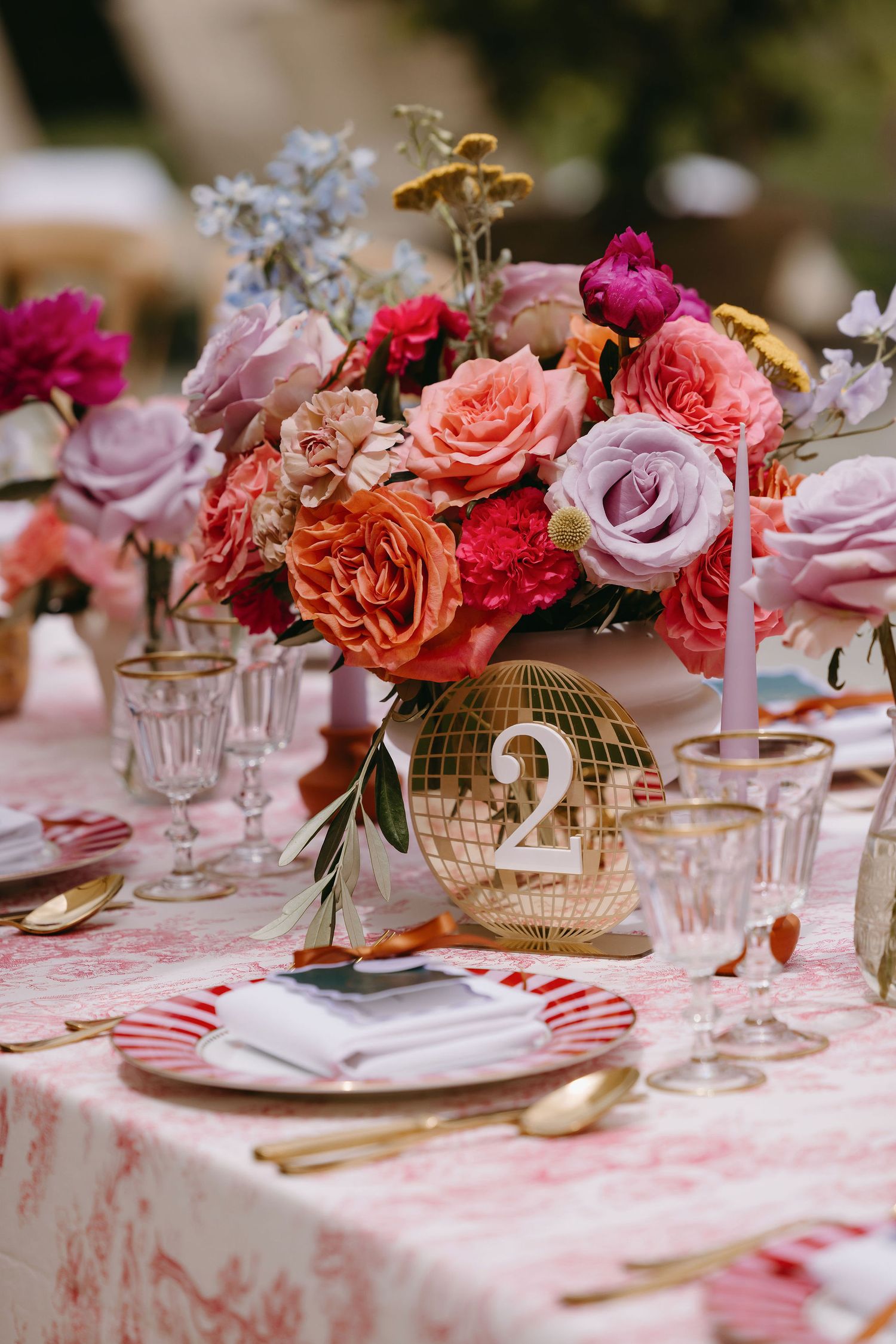 Elegant table setting with pink and coral roses in a gold-numbered vase and striped place settings for a special occasion.
