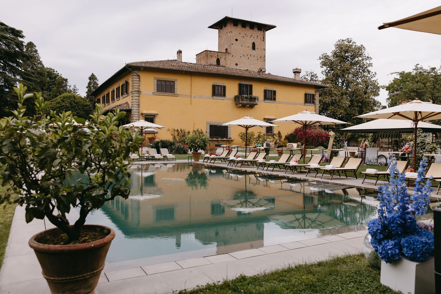 Mediterranean villa with swimming pool surrounded by lounge chairs and potted plants.