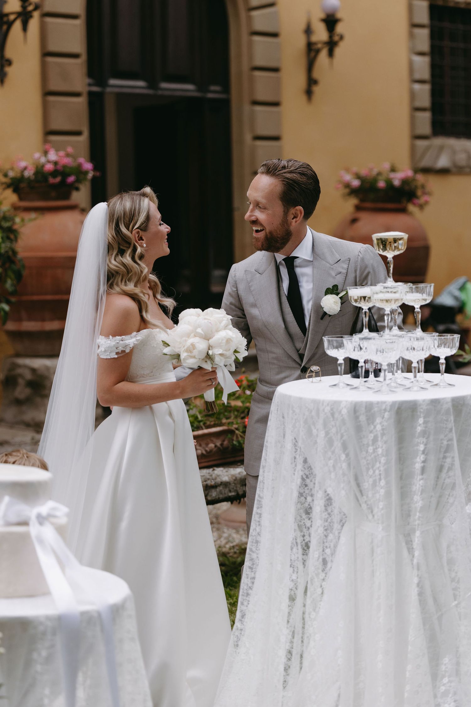Elegant wedding reception setup with champagne tower and white lace tablecloth in garden setting.